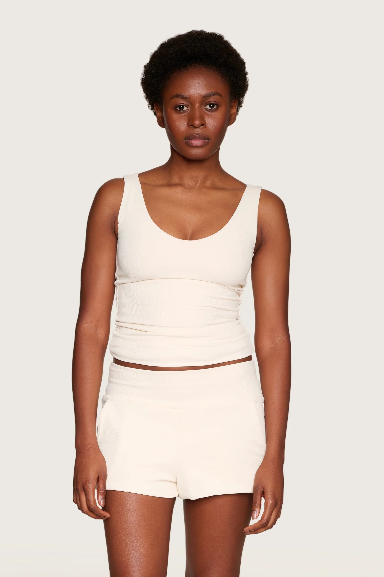 Person trägt MYMARINI Top mit Rundhalsausschnitt und Shorts in Creme vor neutralem Hintergrund.#color_off-white