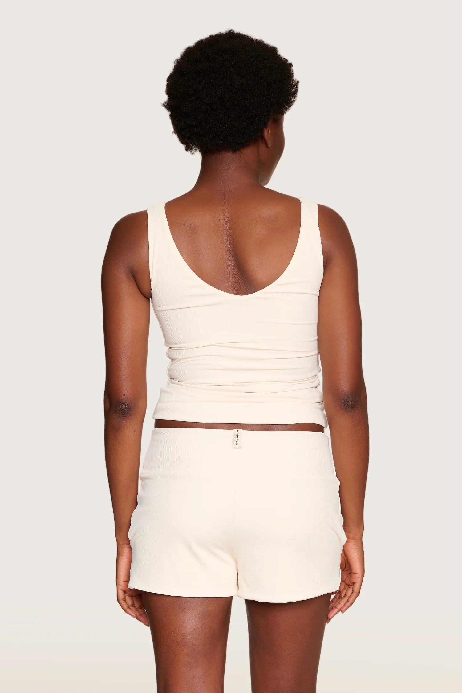 Person von hinten in cremefarbenem MYMARINI-Top mit V-Ausschnitt und breiten Trägern.#color_off-white