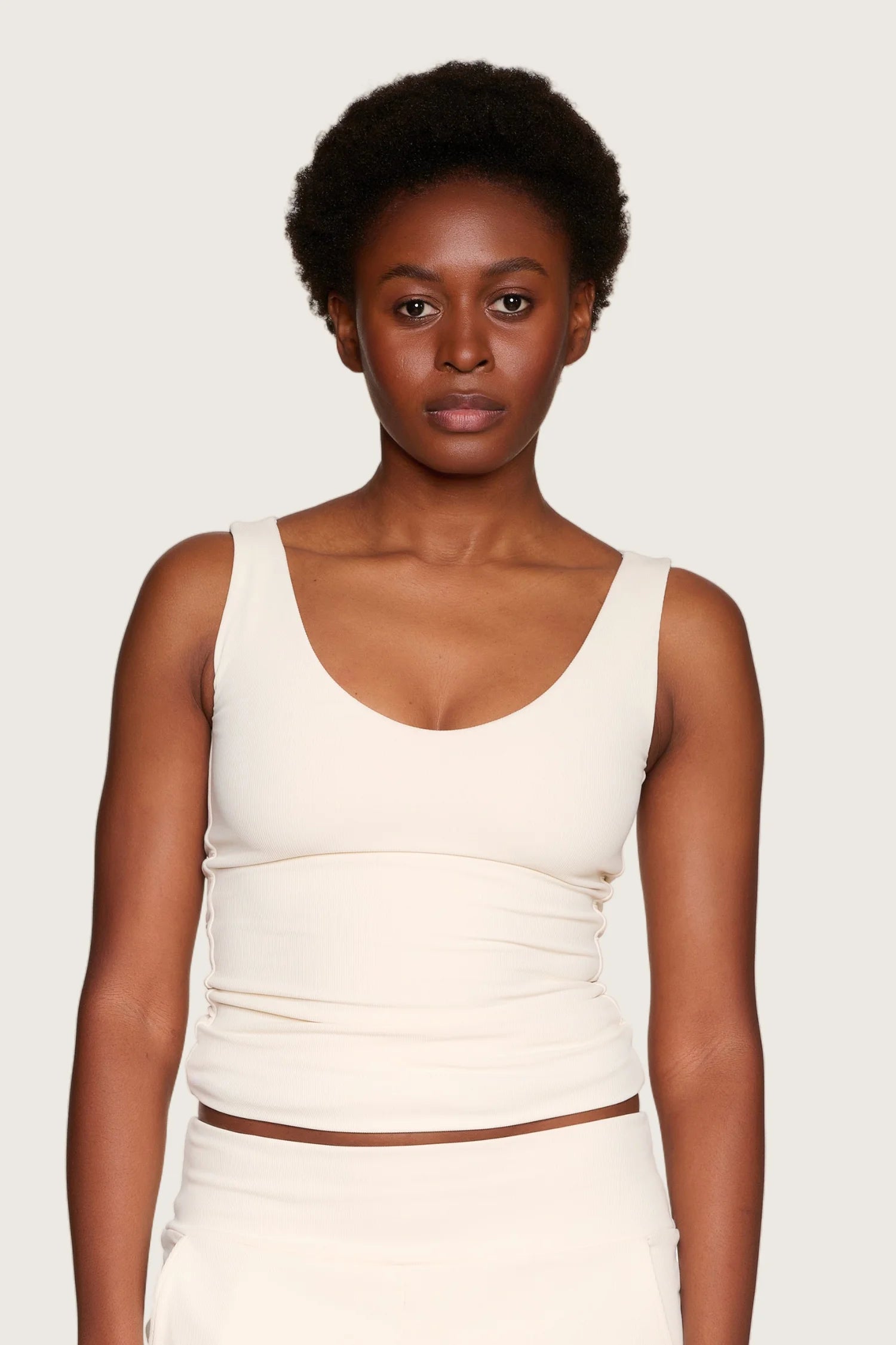 Frau trägt MYMARINI Top mit V-Ausschnitt in Creme.#color_off-white