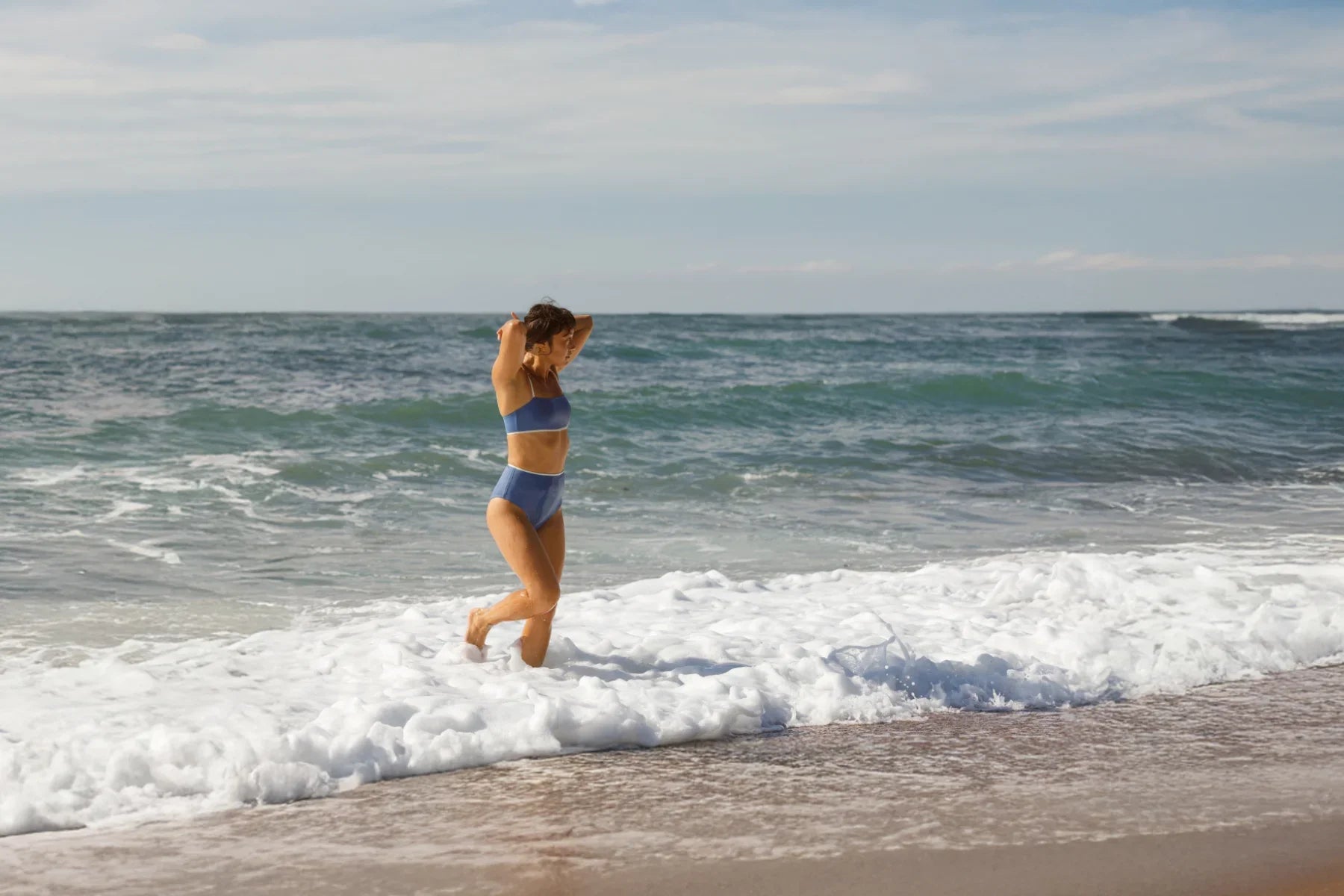 Frau im blauen Sport-Bikini läuft durch Meeresbrandung.