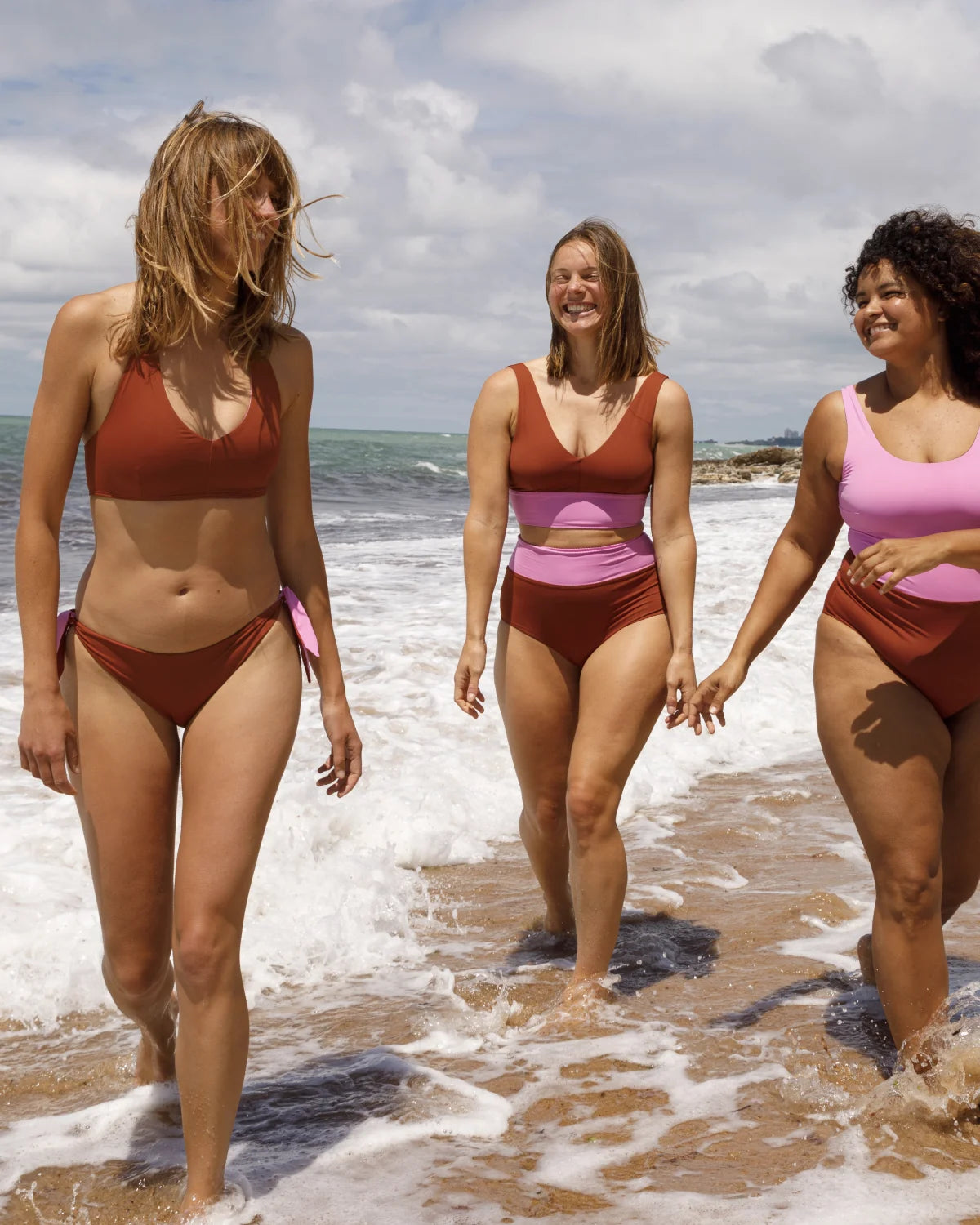 Drei Frauen am Strand tragen MYMARINI Bikinis mit breiten Trägern und hohem Beinausschnitt, lächelnd im Wasser.
