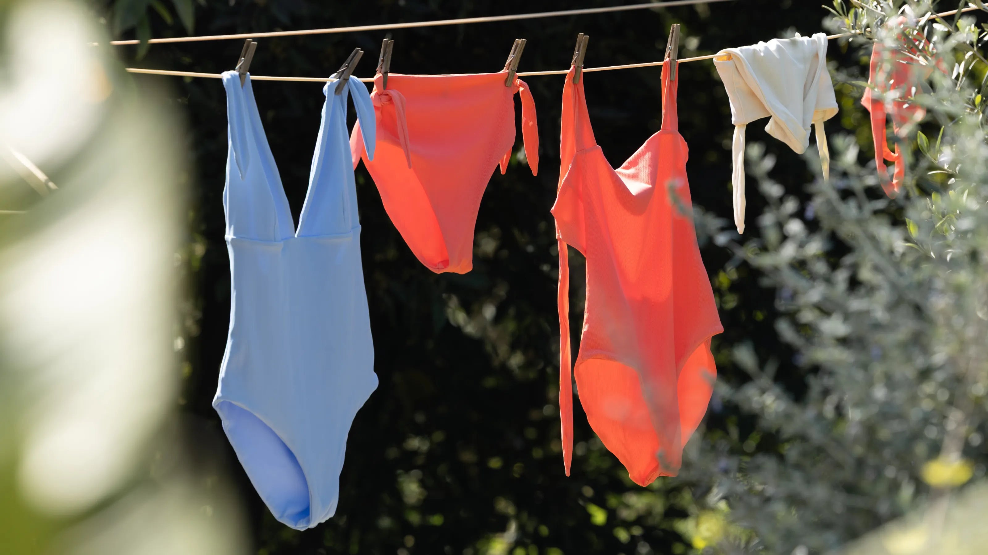 MYMARINI One-Piece: blauer und oranger Badeanzug sowie ein weißes Teil an der Wäscheleine im Garten.