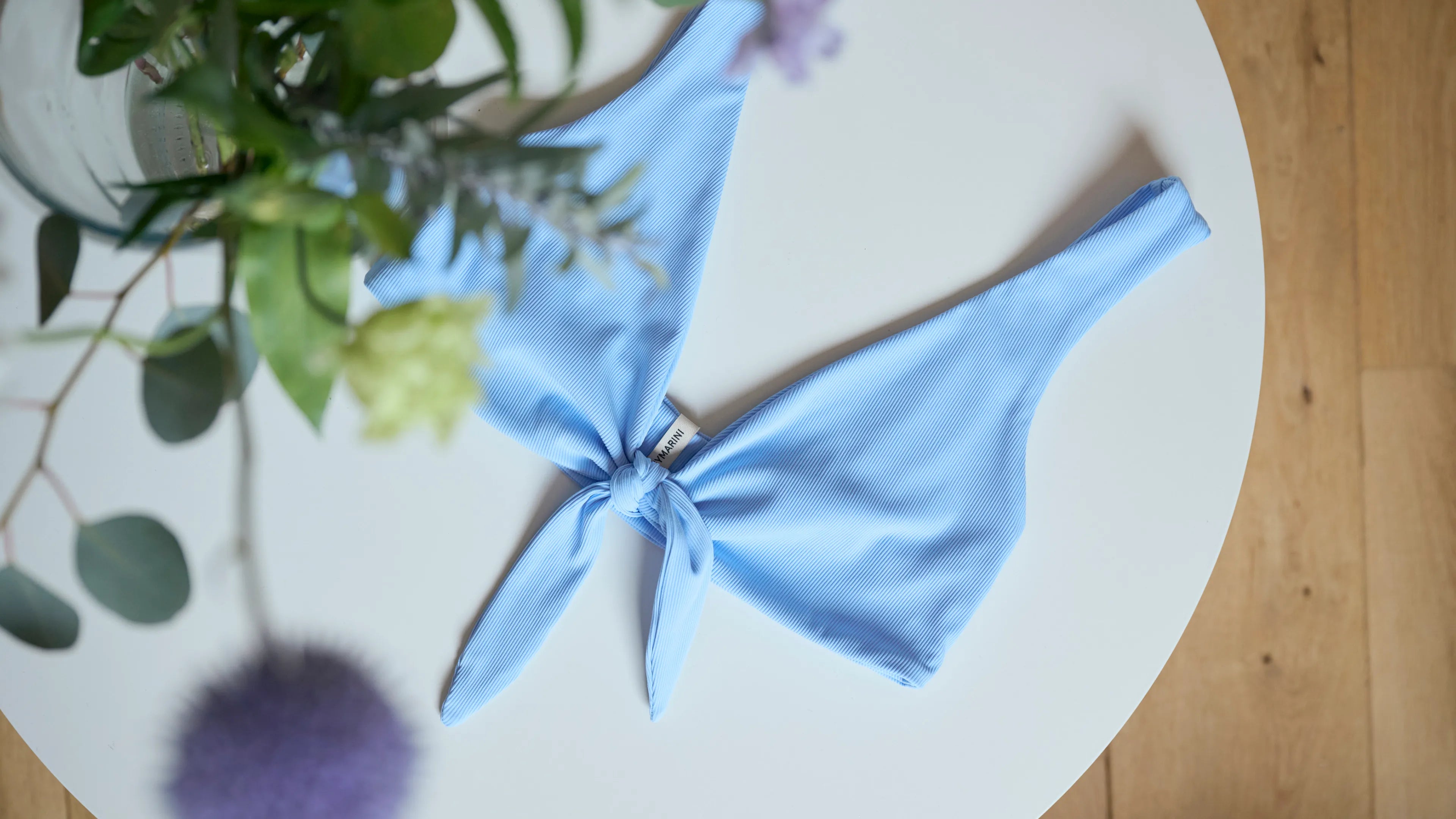 MYMARINI Bikinitop, hellblau gestreift, V-Ausschnitt mit Knoten vorn, auf weißem Teller.