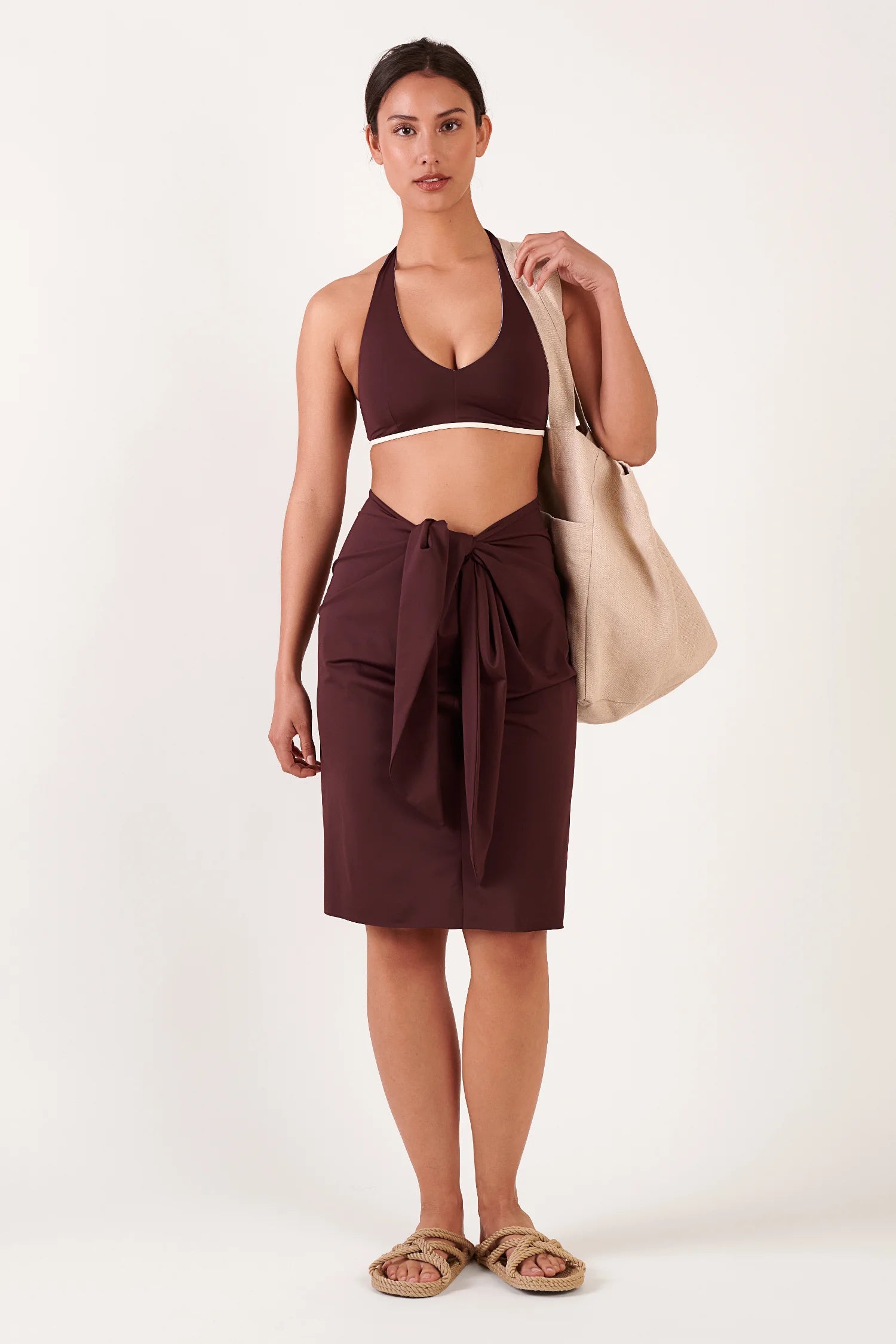 MYMARINI Bikini-Top (Neckholder) und Wickelrock in Dunkelbraun; beige Tragetasche und Sandalen ergänzen das Outfit.#color_chocolate
