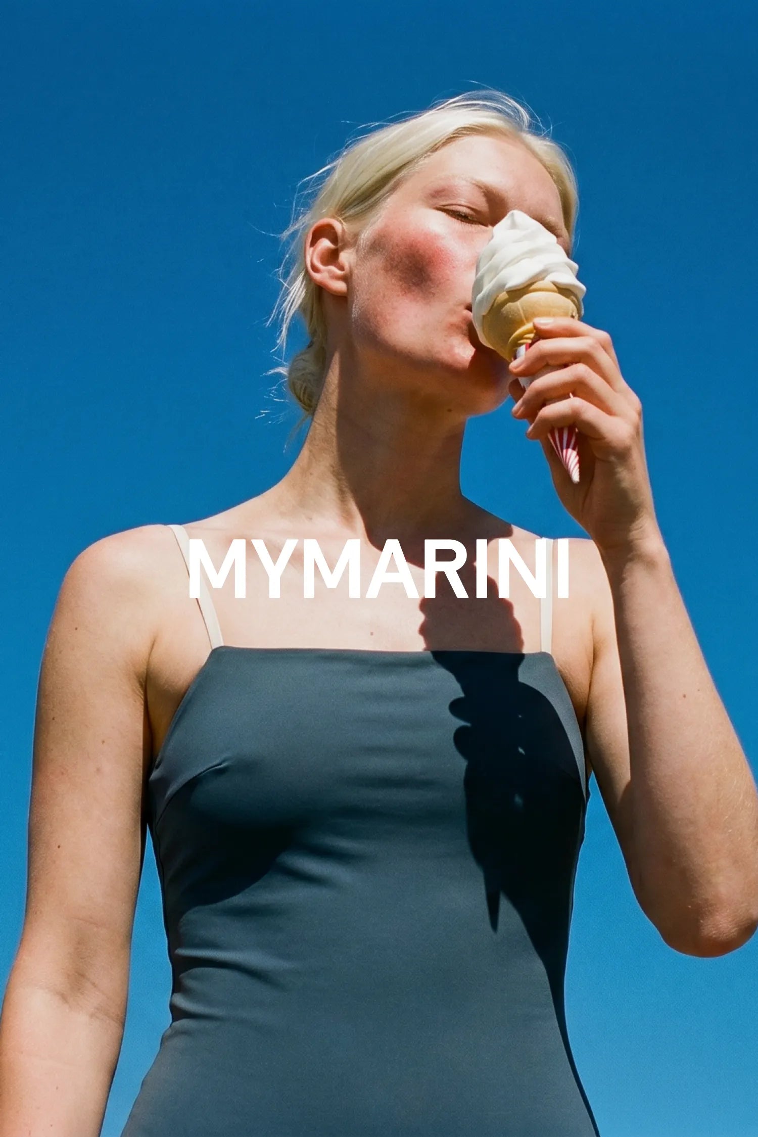 AI-generated, blonde woman against a blue sky eating soft-serve ice cream in grey swimwear, MYMARINI wordmark