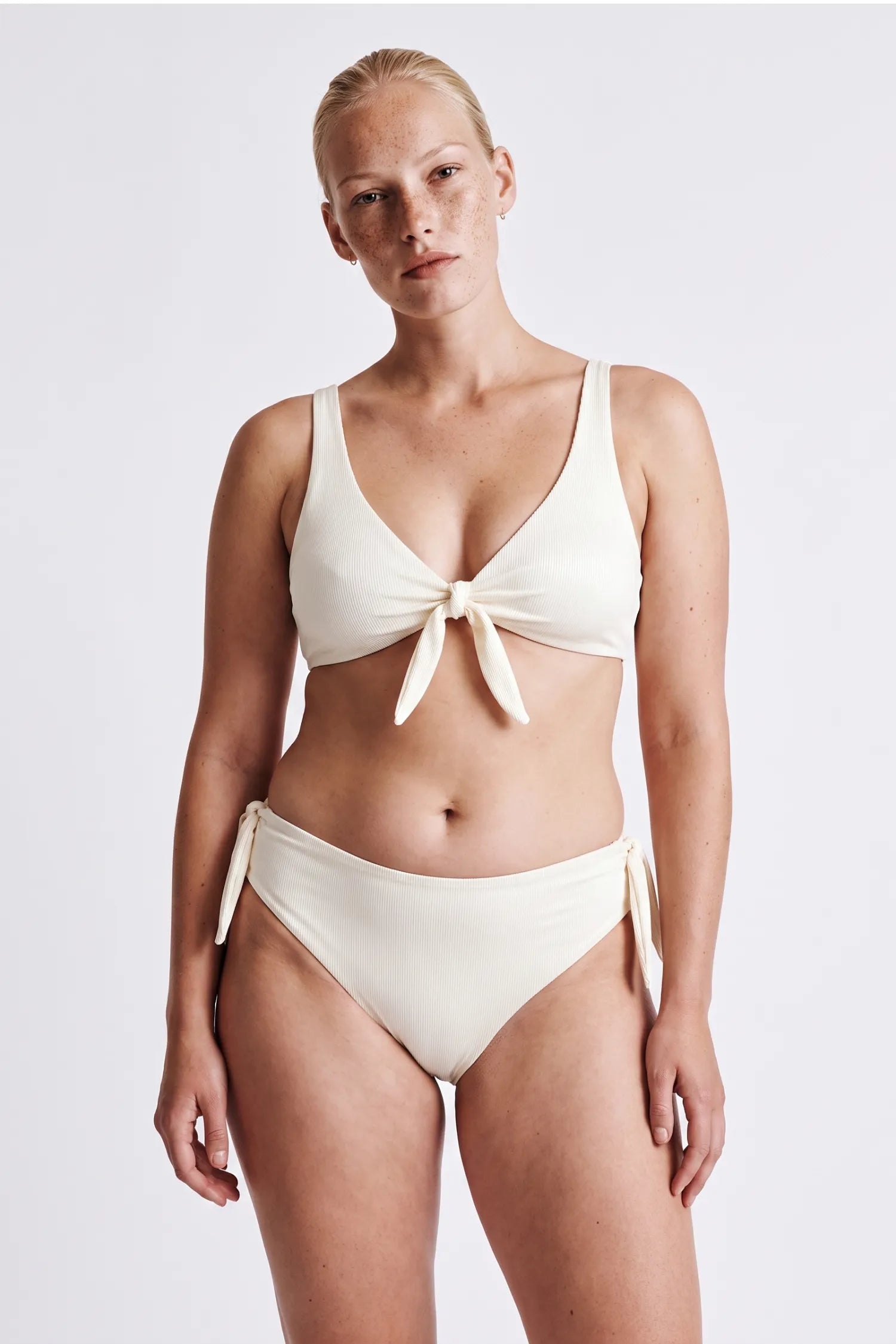 AI-generated, woman wearing the MYMARINI BOW SET bikini in cream, front-tie top and high-waist bottom with side ties