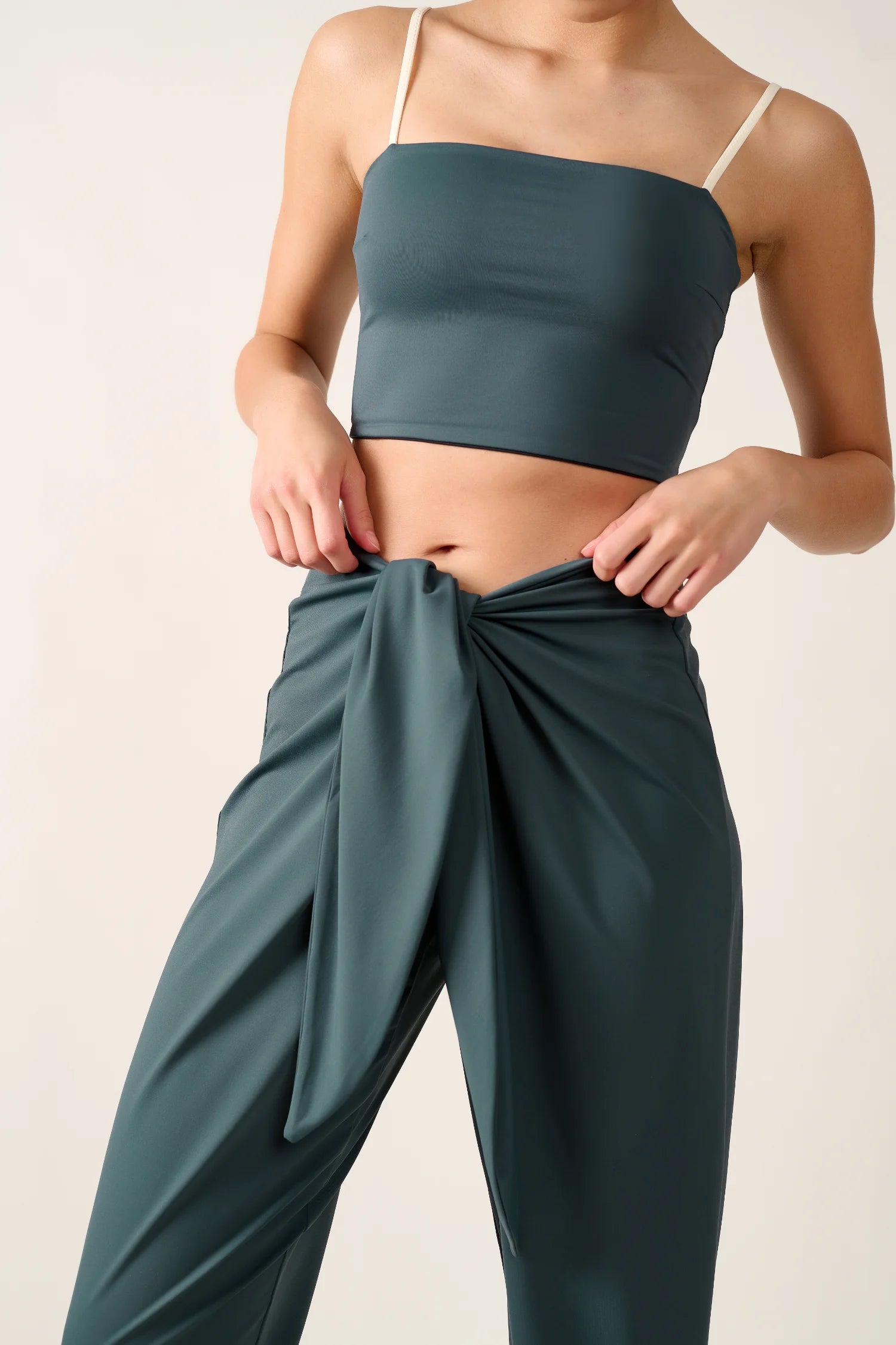 Frau trägt ein MYMARINI Bikinitop mit Spaghettiträgern und eine locker gebundene Hose.#color_grey
