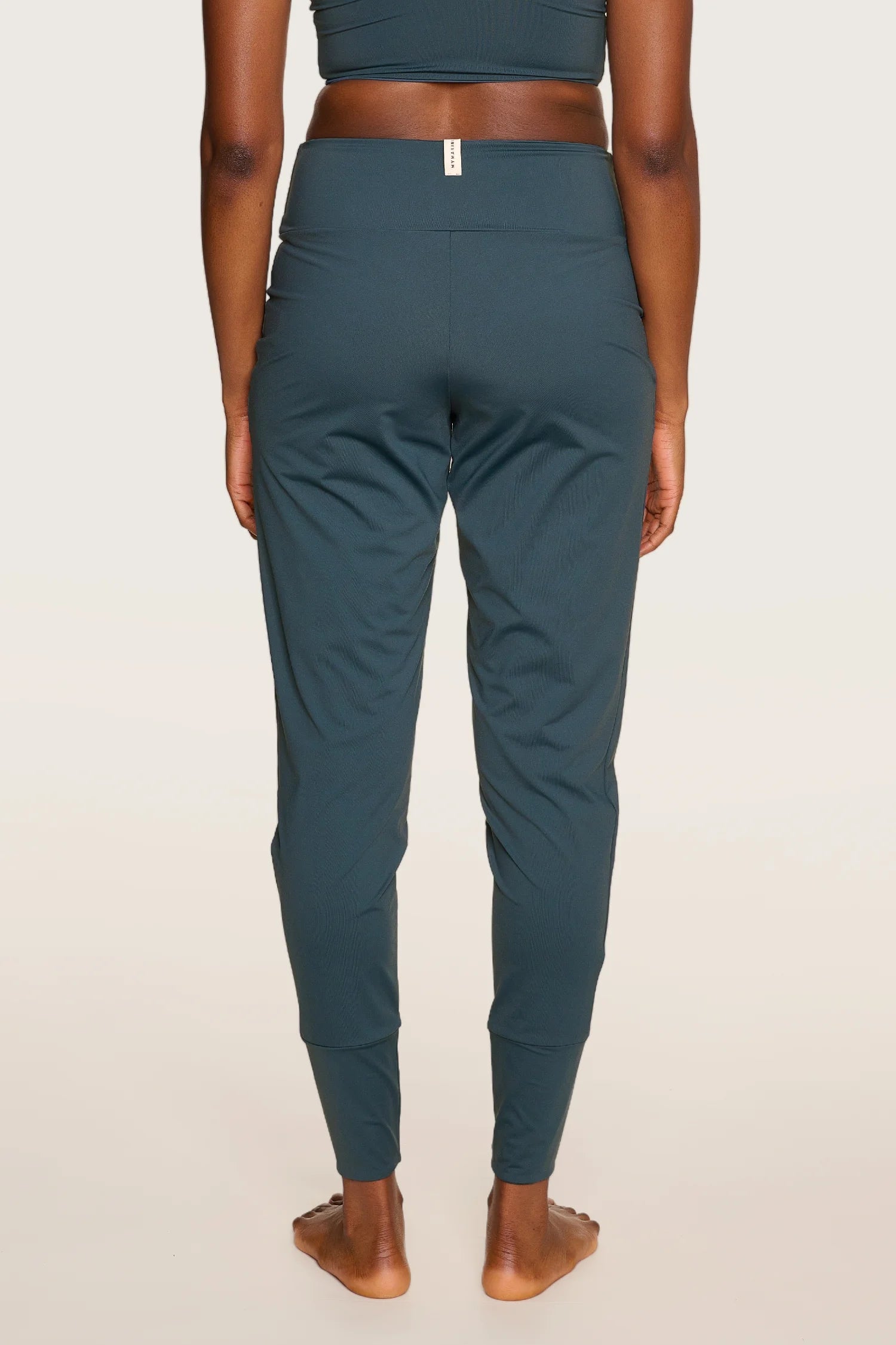 Person trägt MYMARINI-Hose in Dunkelgrün, schmal geschnitten, mit elastischem Bund, von hinten gesehen.#color_grey