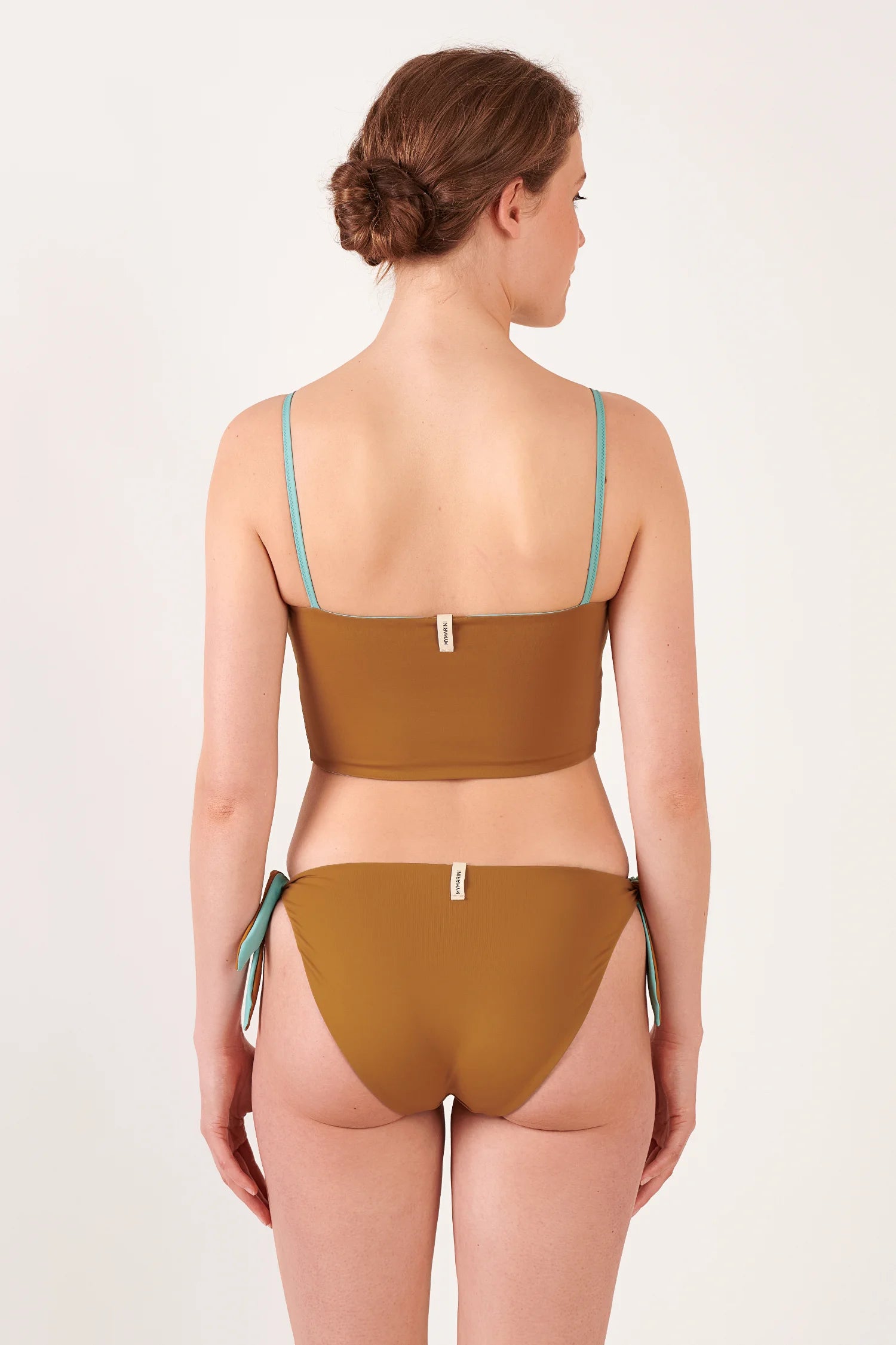 Rückansicht einer Frau in MYMARINI Bikini: braunes Bandeau-Top mit türkisen Trägern und passende Bikinihose mit Seitenschnürungen; Logo-Label sichtbar.#color_oak-eucalyptus