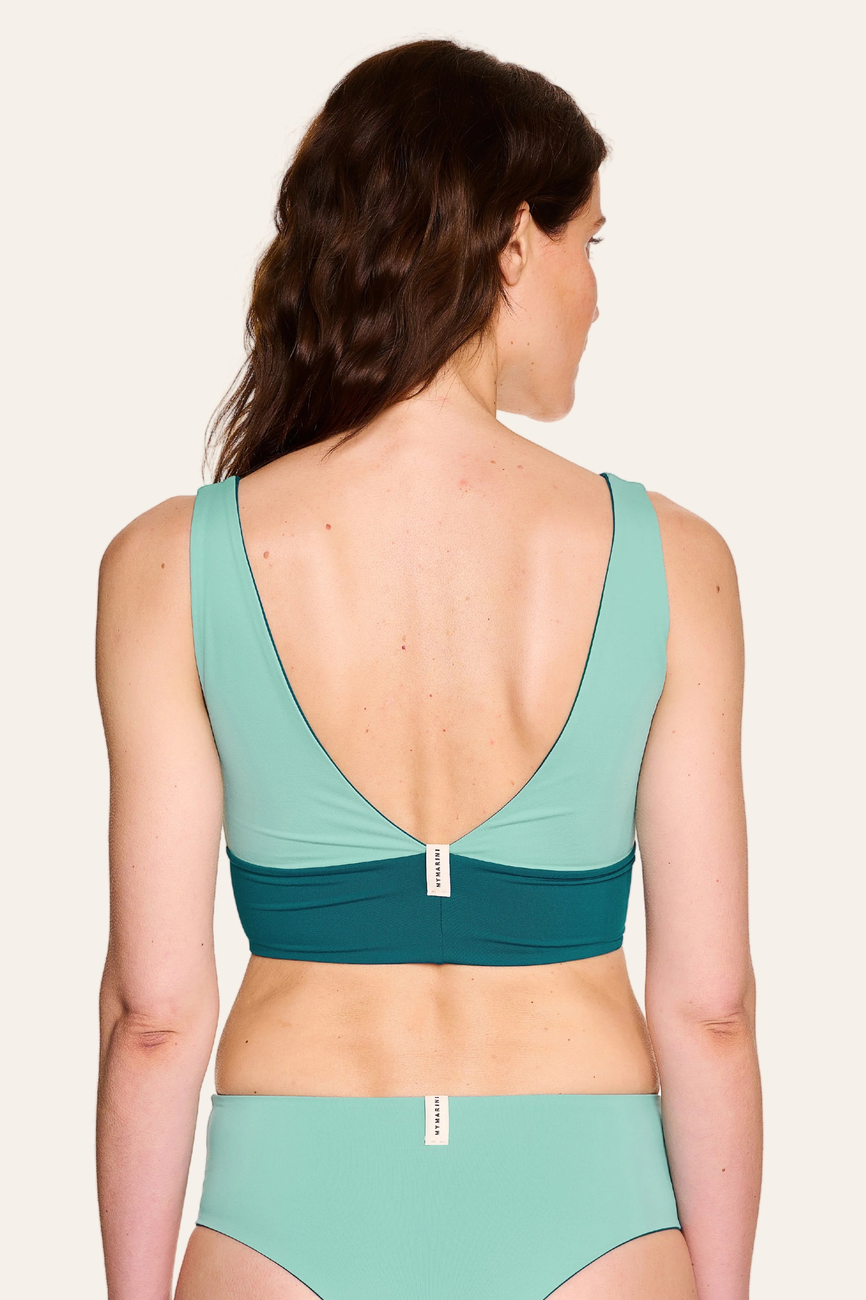 Rückansicht einer Frau in einem MYMARINI Bikinitop mit V-Ausschnitt und einer Bikinihose, beide in Grün.#color_eucalyptus-petrol