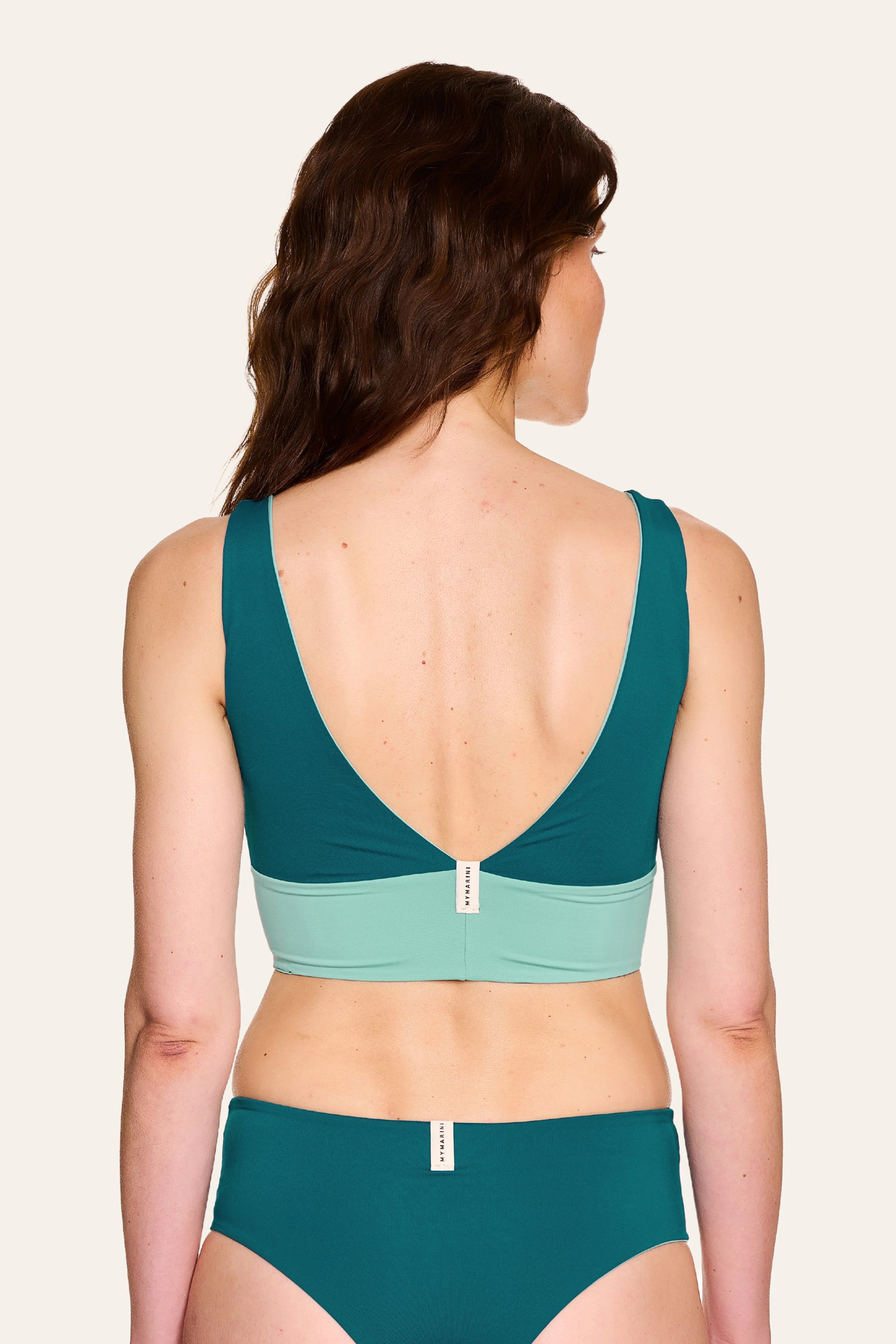 Frau trägt MYMARINI Bikinitop mit tiefem Rückenausschnitt und Bikinihose in Türkis und Mint.#color_eucalyptus-petrol