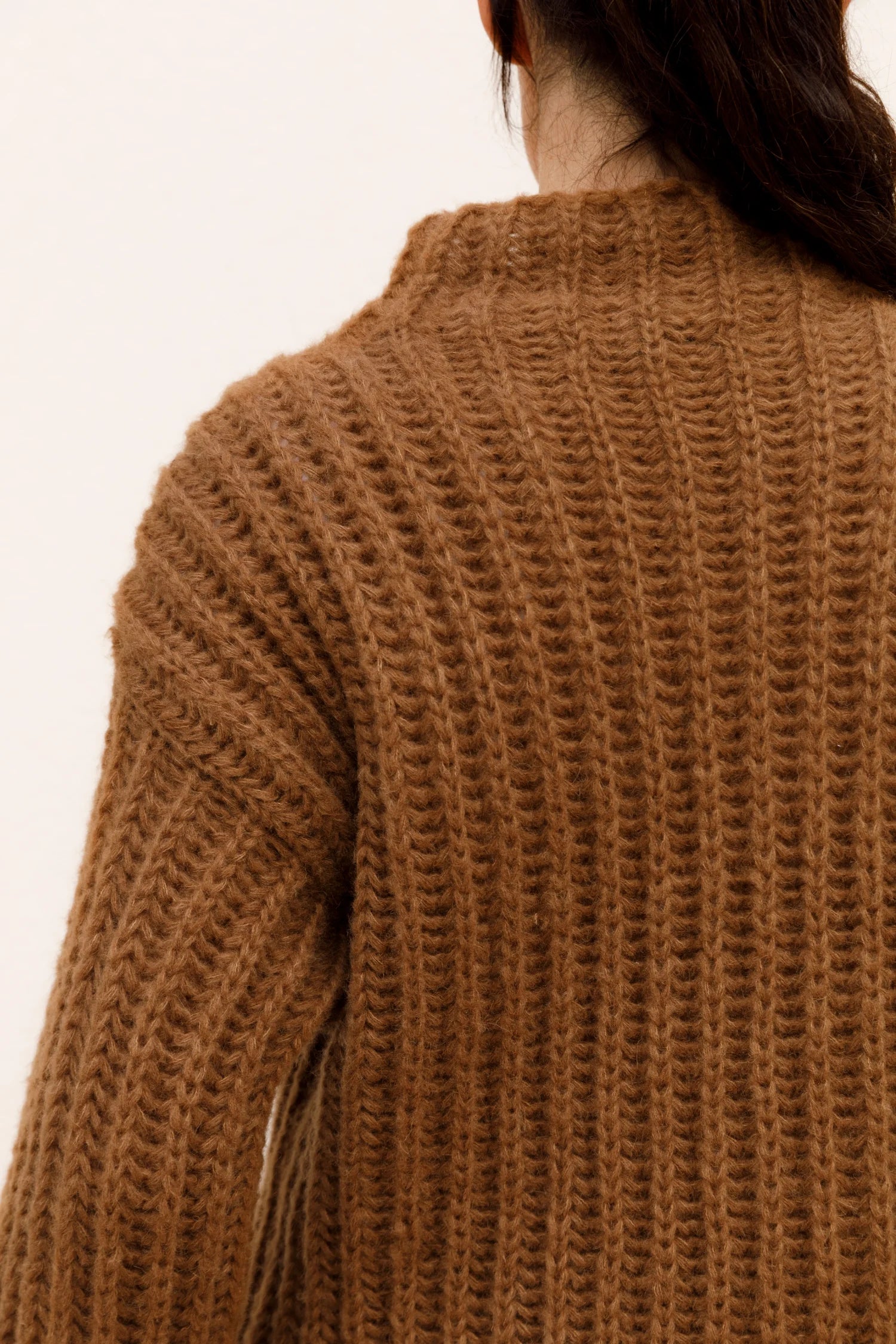 Rückansicht einer Person in einem grob gestrickten, braunen Pullover von MYMARINI.#color_camel