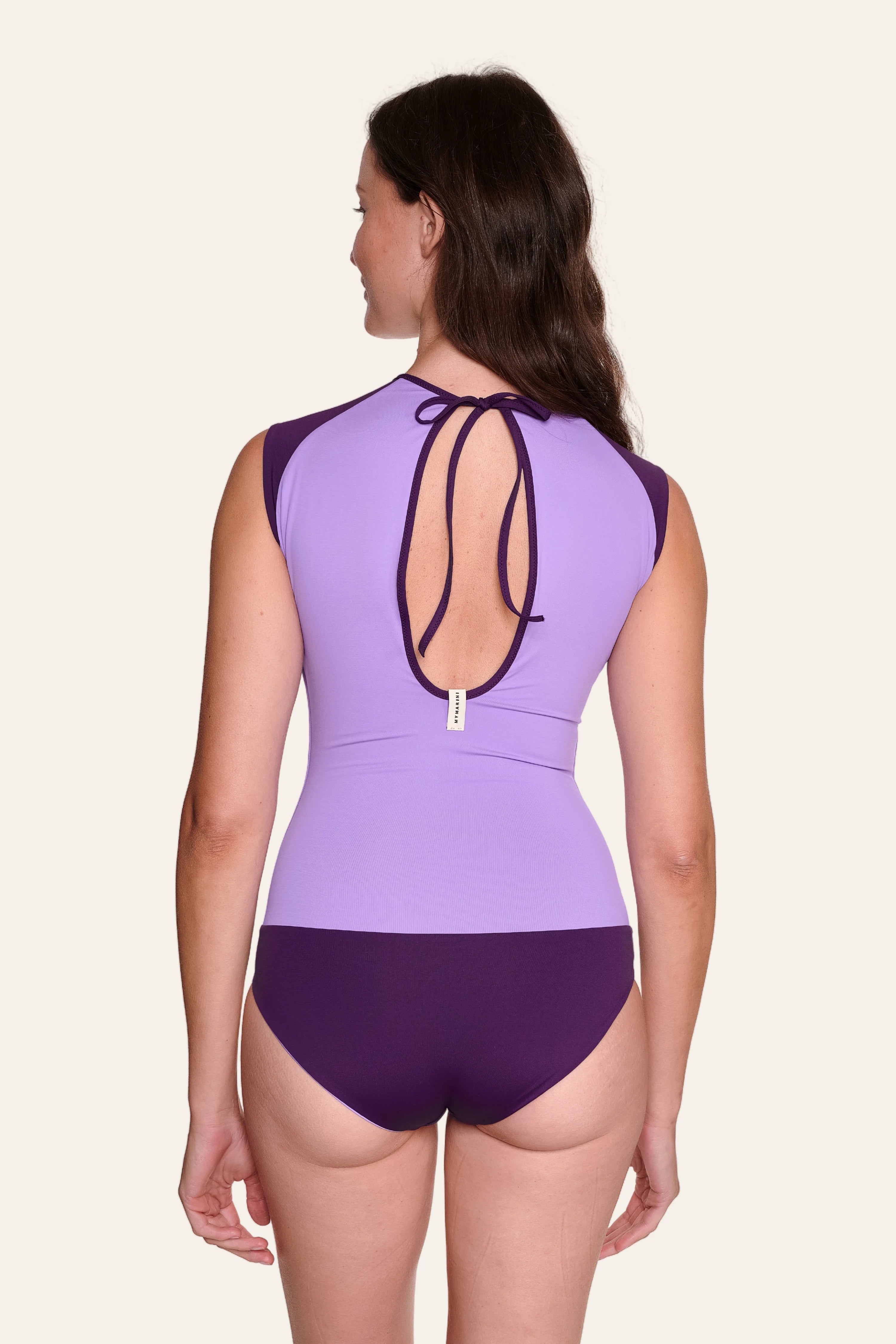 Frau in lila MYMARINI Badeanzug mit hohem Beinausschnitt und tiefem Rückenausschnitt, von hinten.#color_lavender-plum