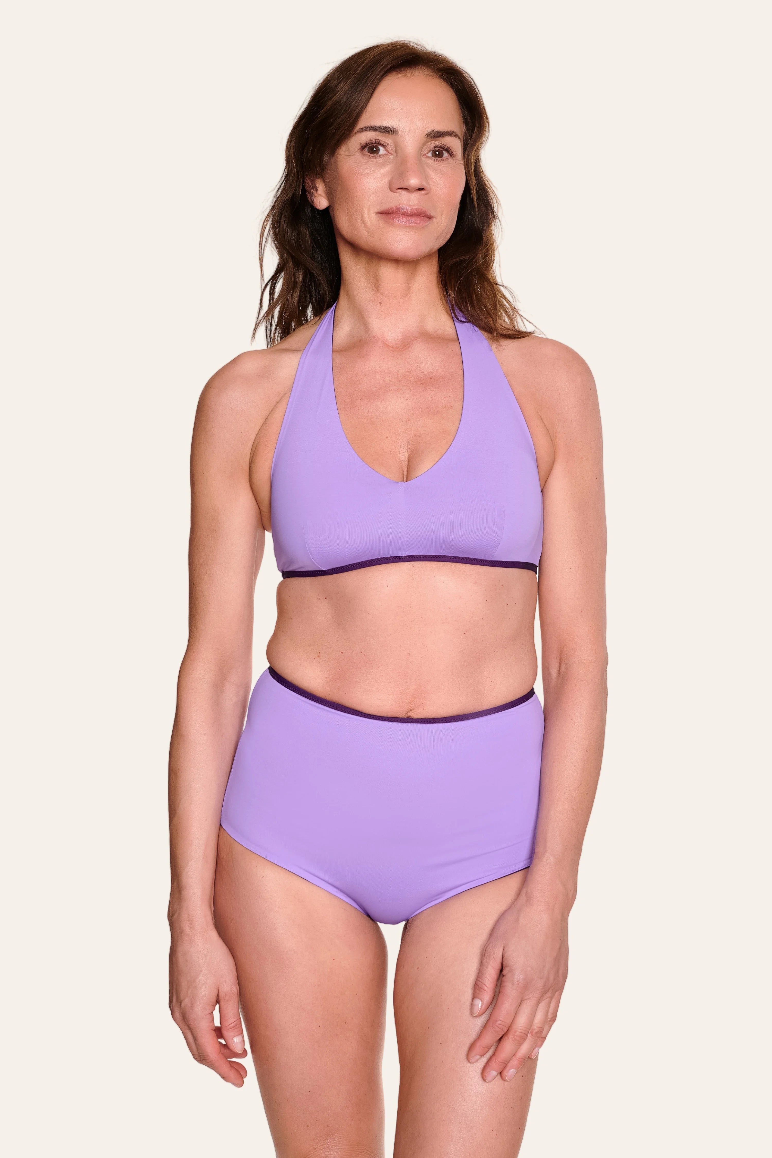 Frau trägt lila MYMARINI Neckholder-Bikinitop und High-Waist-Bikinihose vor hellem Hintergrund.#color_lavender-plum