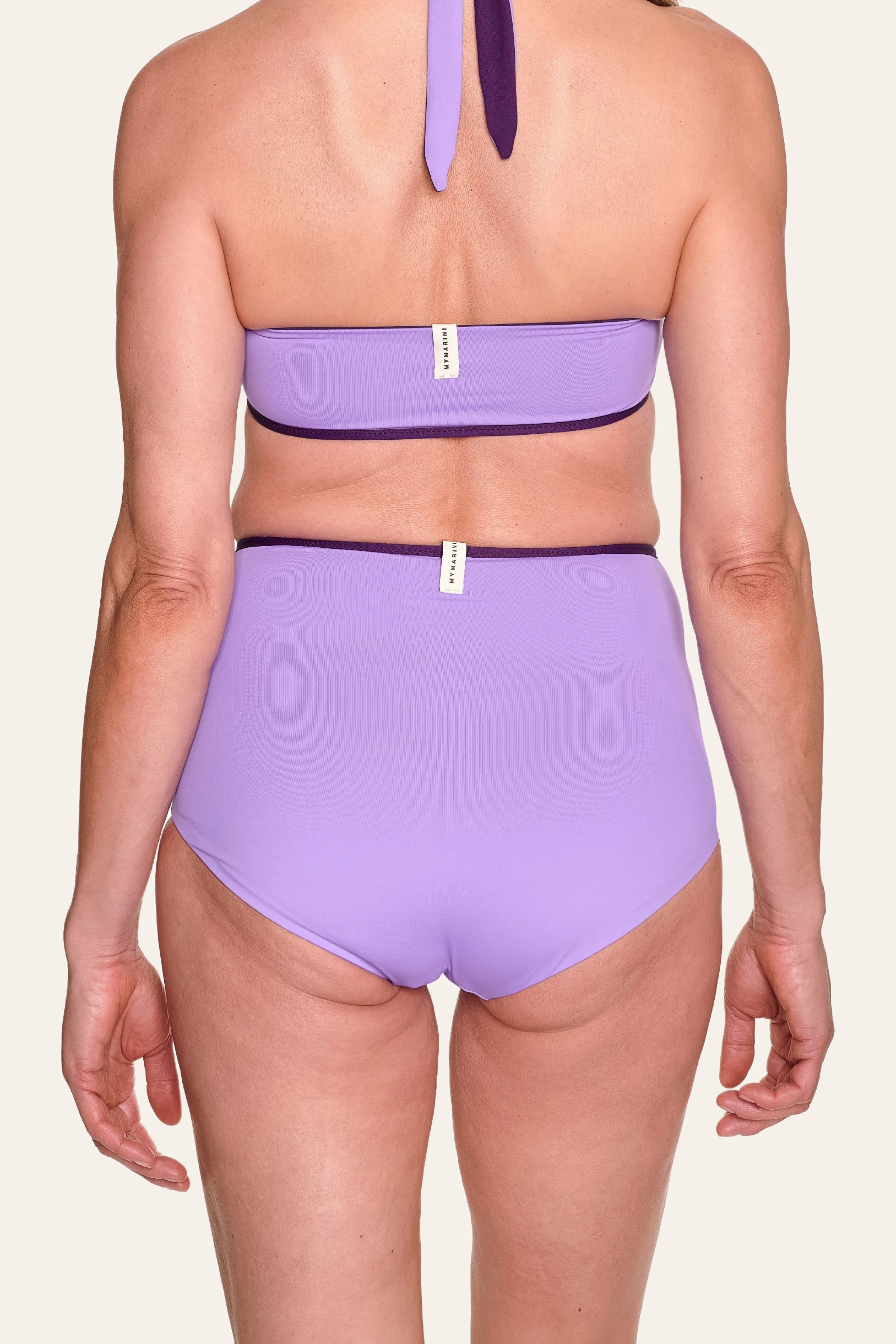 Rückansicht einer Person in einem lila MYMARINI Bikini mit Bandeau-Top und High-Waist-Hose.#color_lavender-plum
