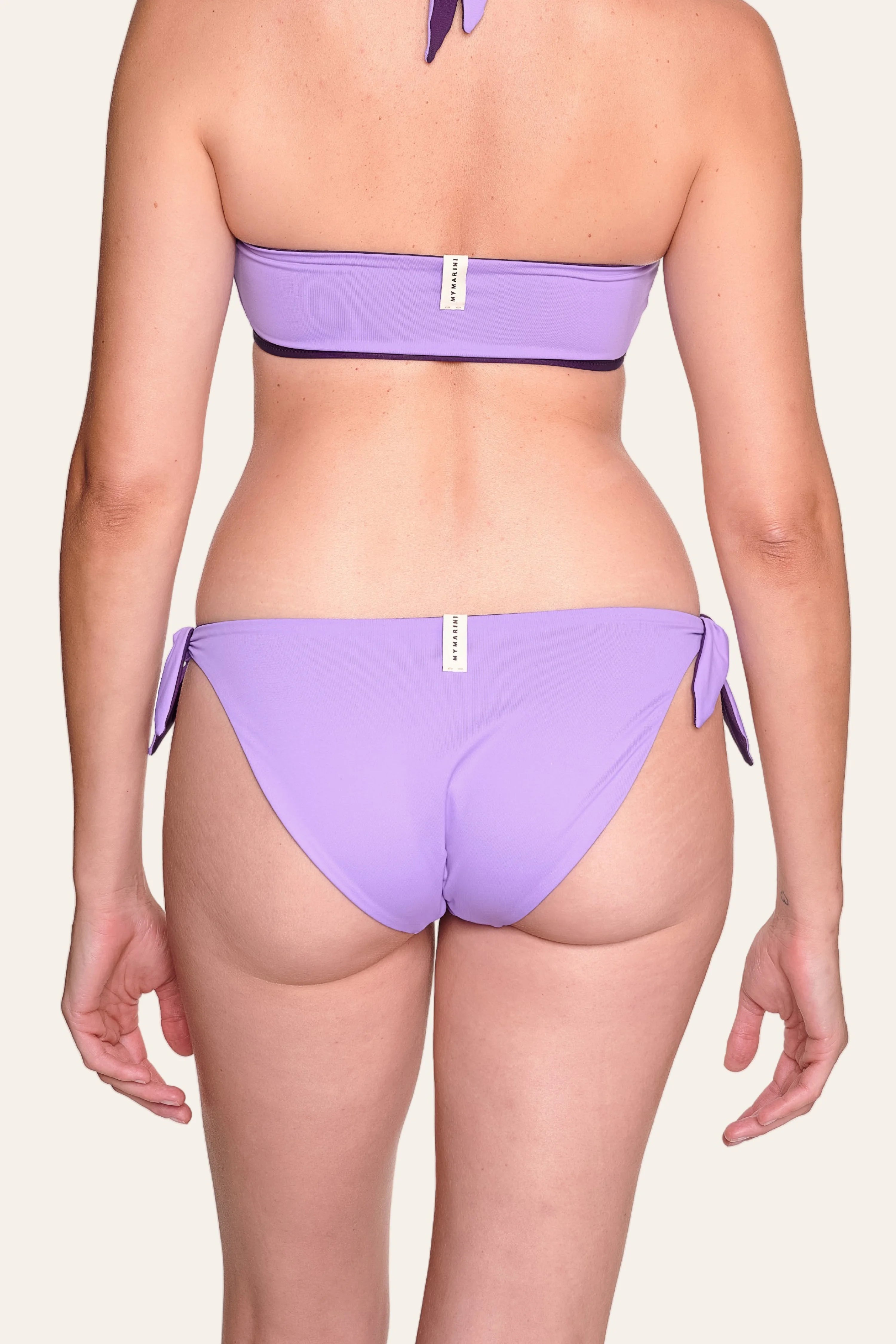 Frau trägt lila MYMARINI Bikinihose mit hohem Beinausschnitt und Bandeau-Top, Rückansicht.#color_lavender-plum