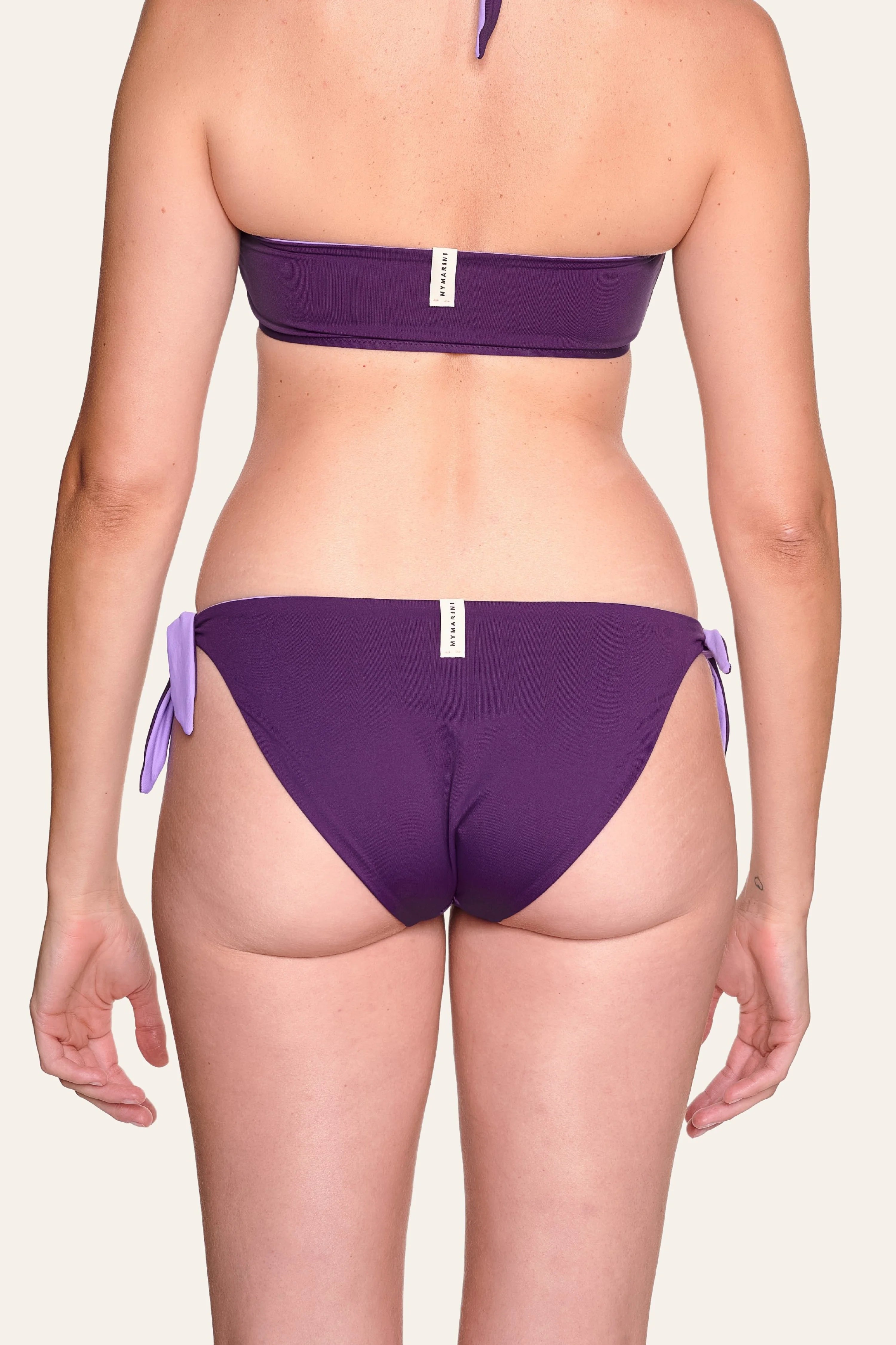 Rückansicht einer Person in MYMARINI Bikinihose mit hohem Beinausschnitt und seitlichen Schleifen in Lila.#color_lavender-plum