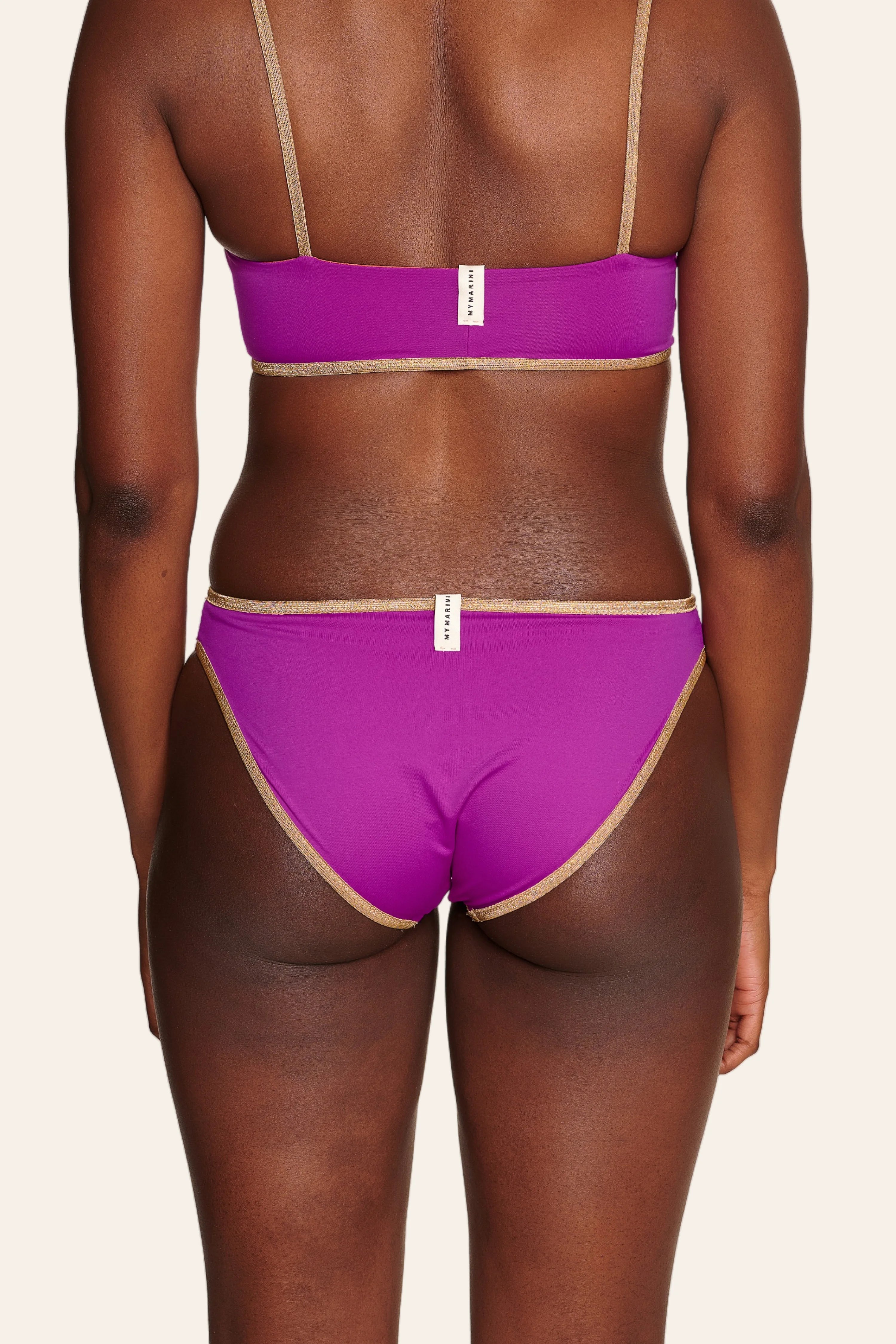 Rückansicht einer Person in einem MYMARINI Bikini mit Spaghettiträgern und hohem Beinausschnitt in Lila.#color_papaya-cassis
