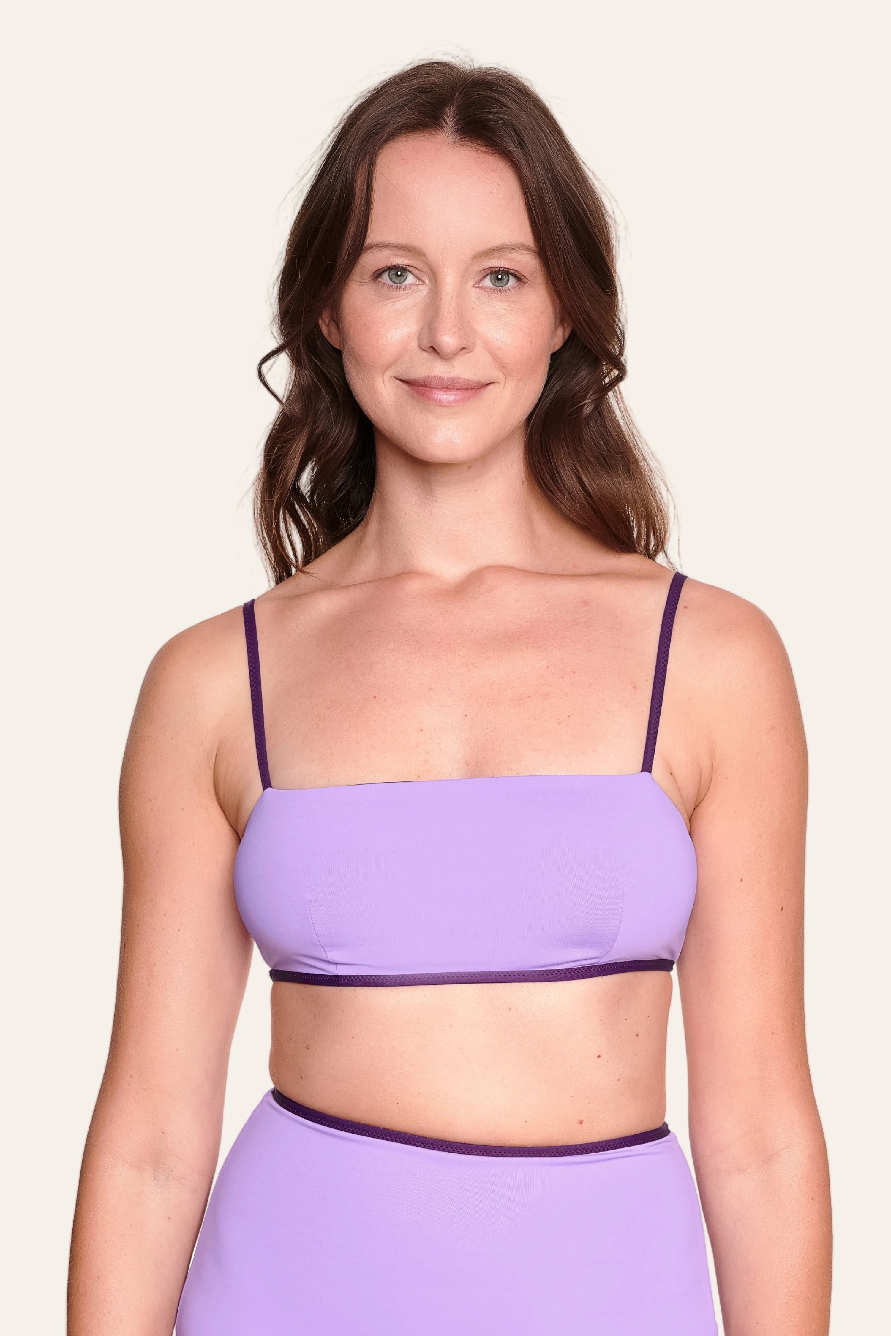 Frau trägt MYMARINI Bikinitop mit Spaghettiträgern und Bikinihose in Lila, vor hellem Hintergrund.#color_lavender-plum