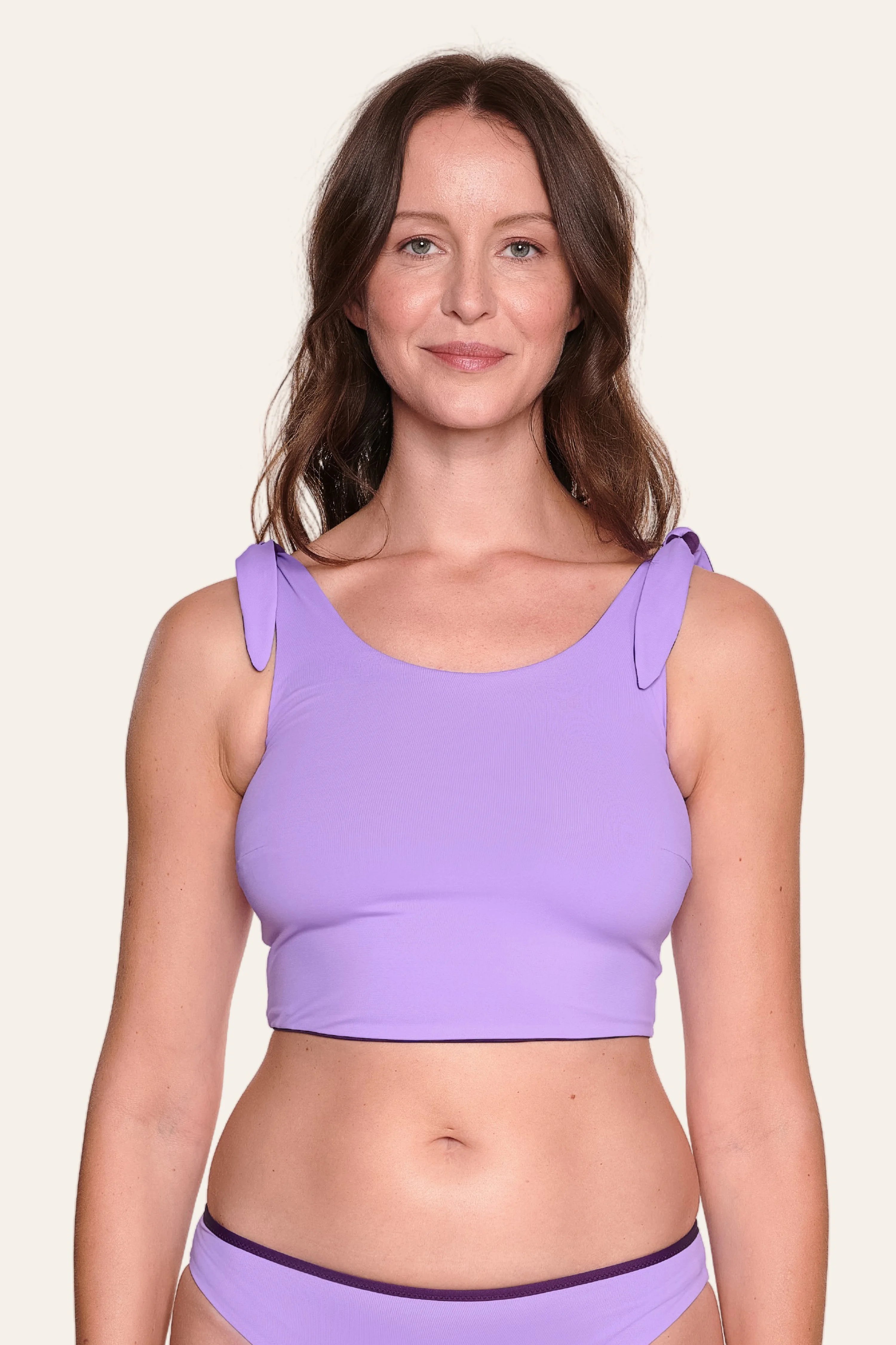 Frau trägt lila MYMARINI Bikinitop mit breiten Trägern und passender Bikinihose vor hellem Hintergrund.#color_lavender-plum