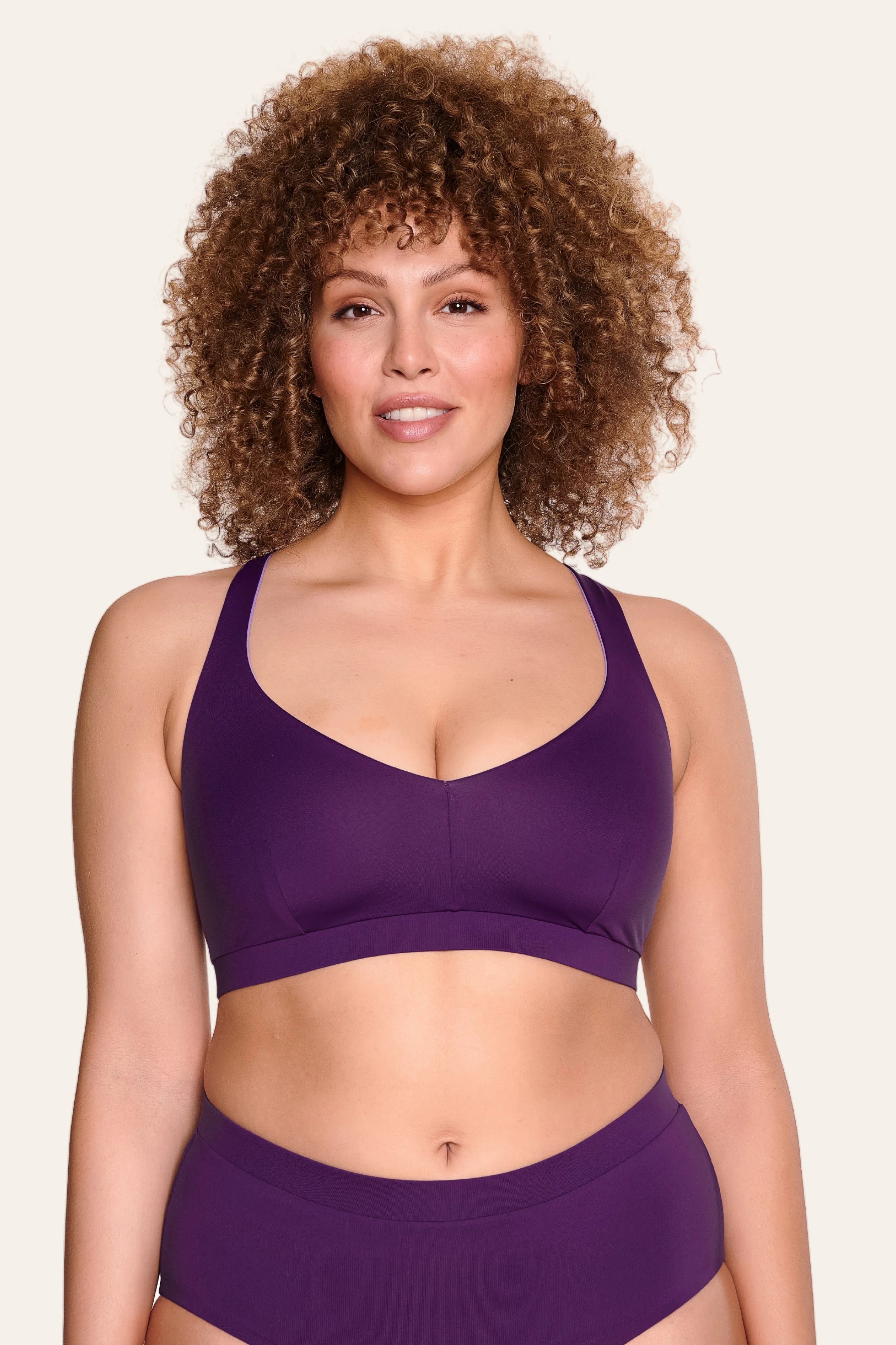 Frau trägt MYMARINI Bikinitop mit V-Ausschnitt und breite Träger in Lila, dazu passende Bikinihose.#color_lavender-plum