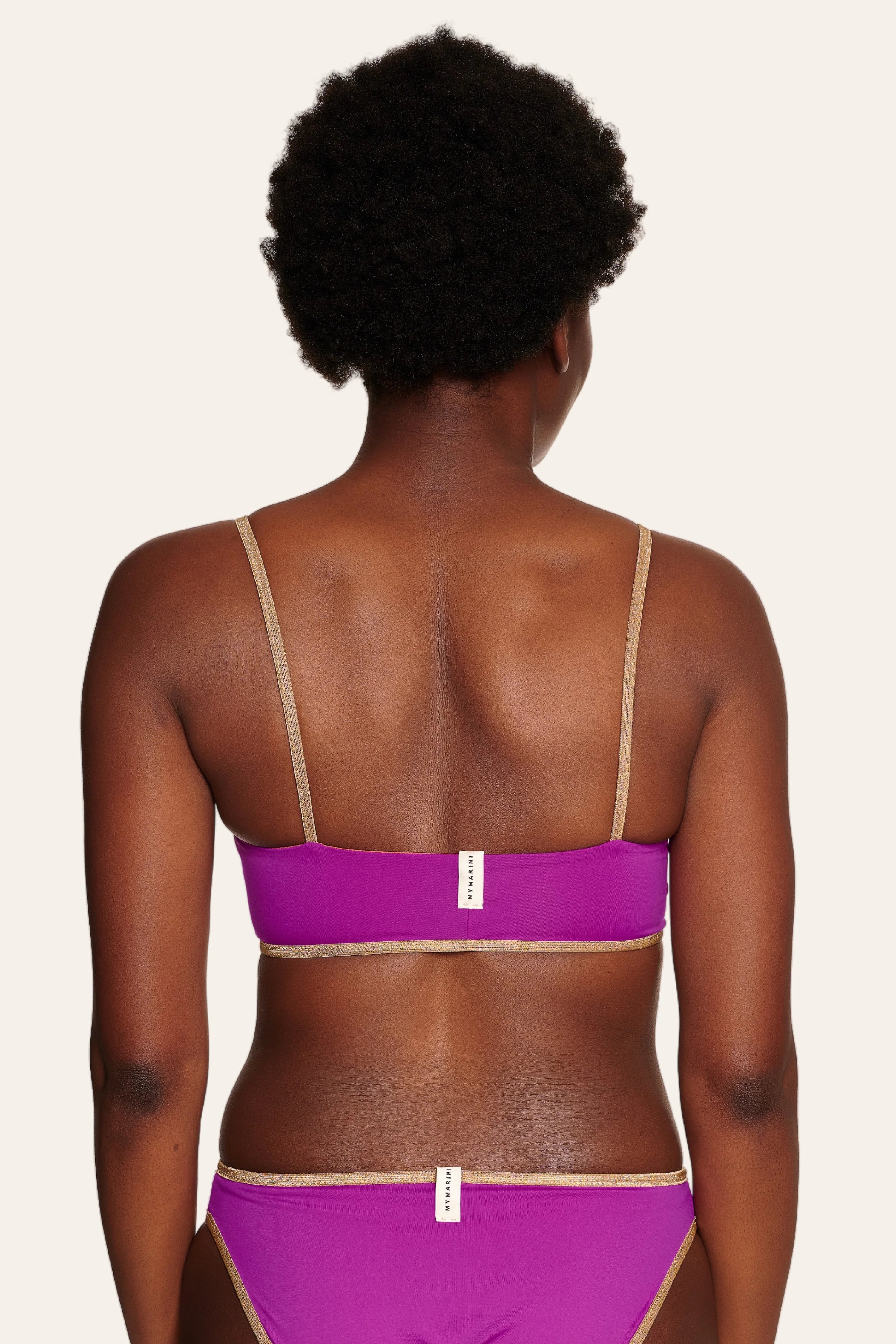 Rückansicht einer Person in einem MYMARINI Bikini mit Spaghettiträgern und Mid rise Schnitt in Lila.#color_papaya-cassis
