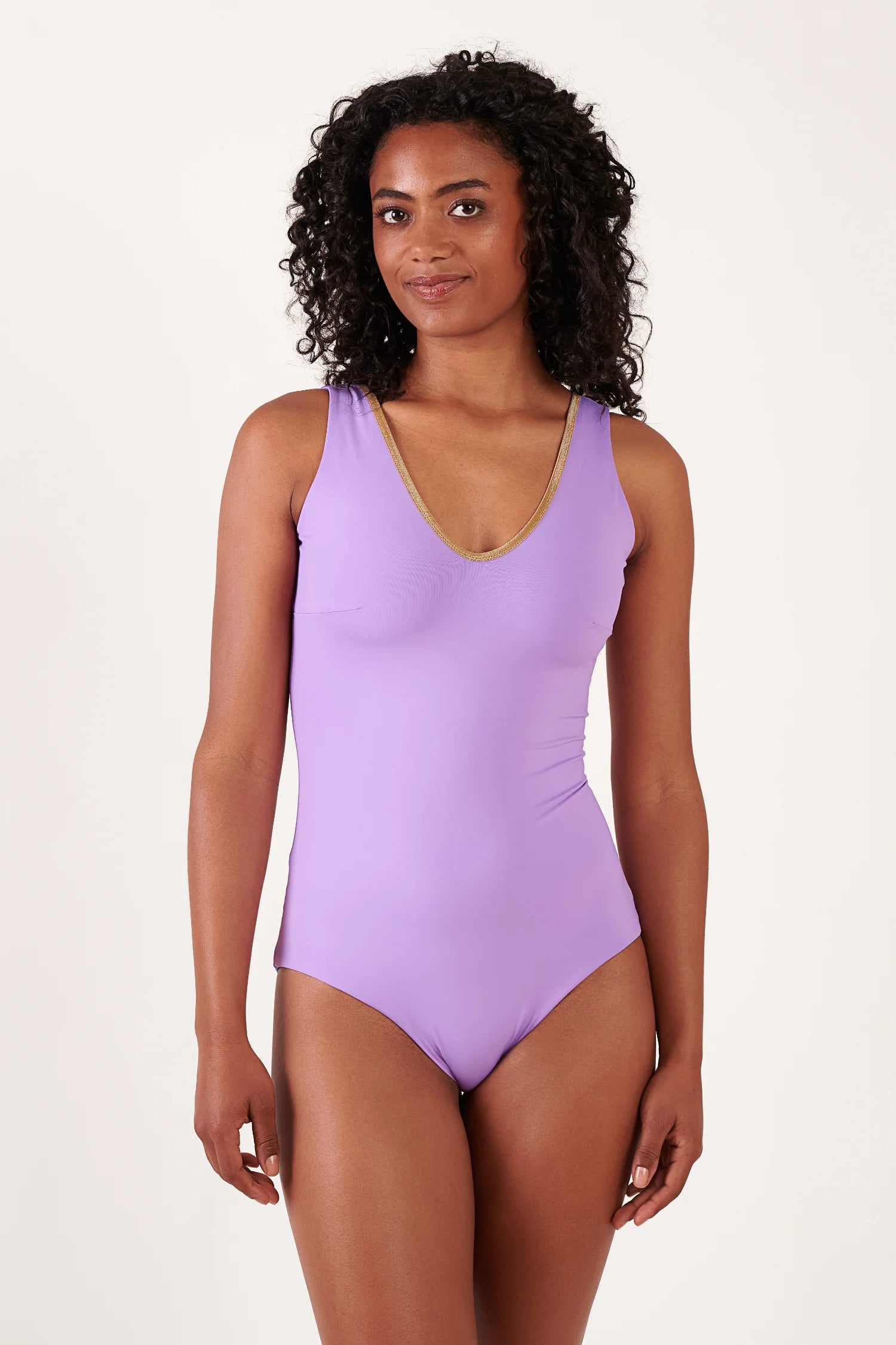 MYMARINI One-Piece Badeanzug in Lavendel/Lila mit V-Ausschnitt und goldnem Rand, von einer Frau mit lockigen Haaren getragen.#color_lapis-lavender