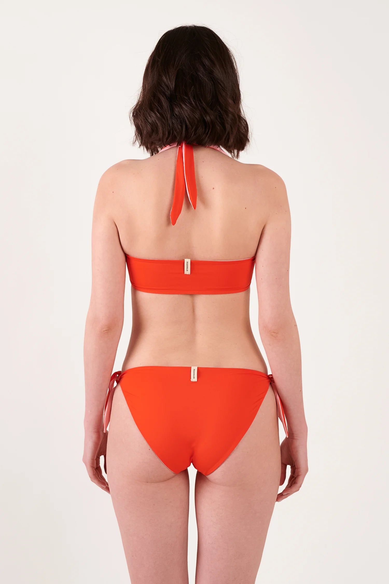 Rückenansicht: orange MYMARINI Bikini mit Neckholder-Top und seitlichen Bindebändern; Label am Ober- und Unterteil sichtbar.#color_poppy-macaron