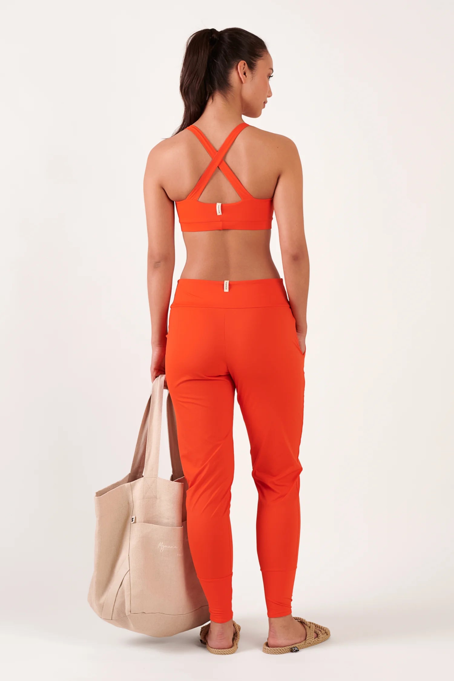 MYMARINI Top und Hose in Orange; Rückenansicht, Kreuz-Träger des Tops, hohes Taillenband der Hose, beige Tote in der Hand.#color_poppy
