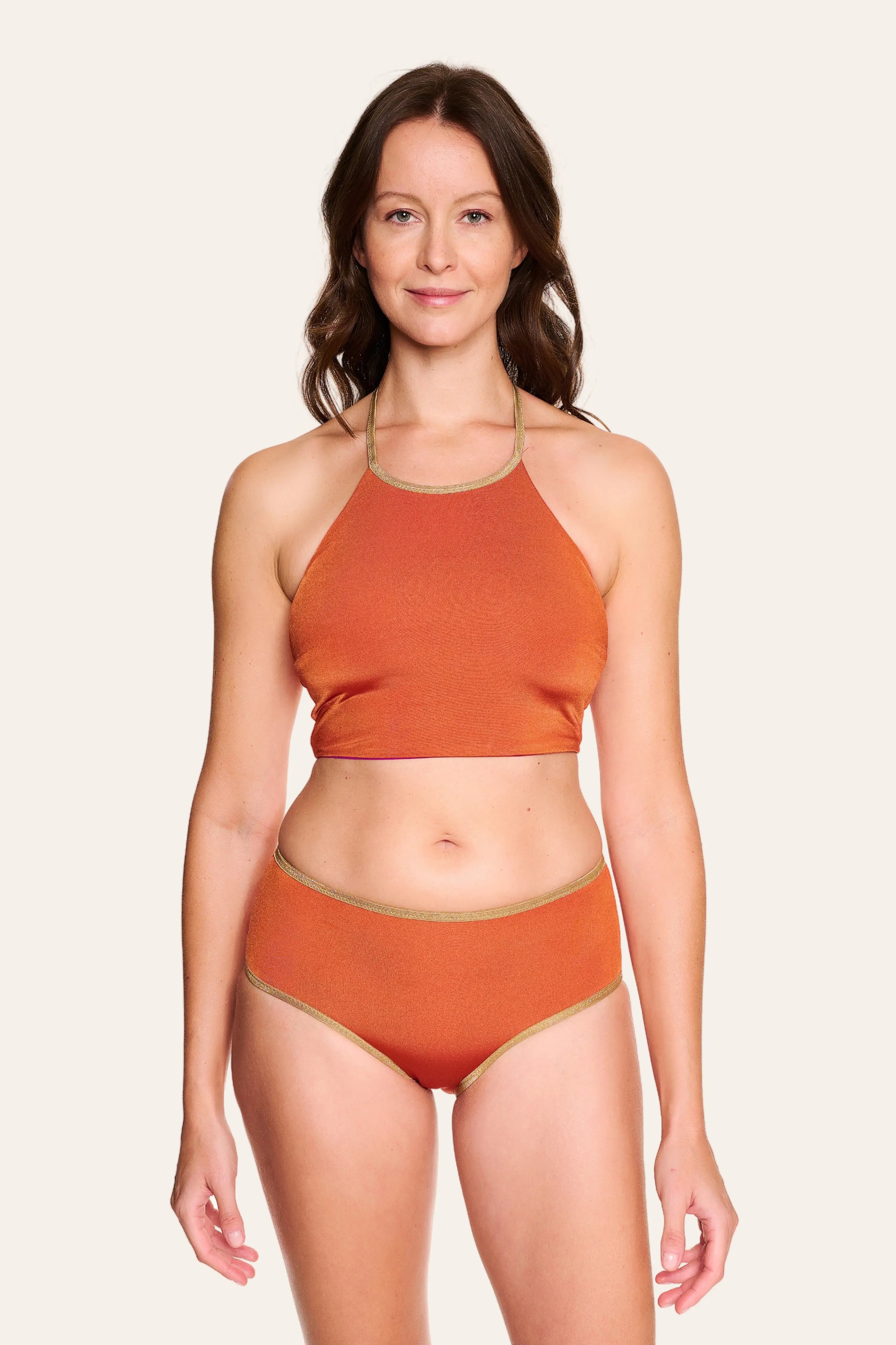 Frau trägt MYMARINI Bikini mit hochgeschlossenem Top und High-Waist-Hose in Orange, vor neutralem Hintergrund.#color_papaya-cassis