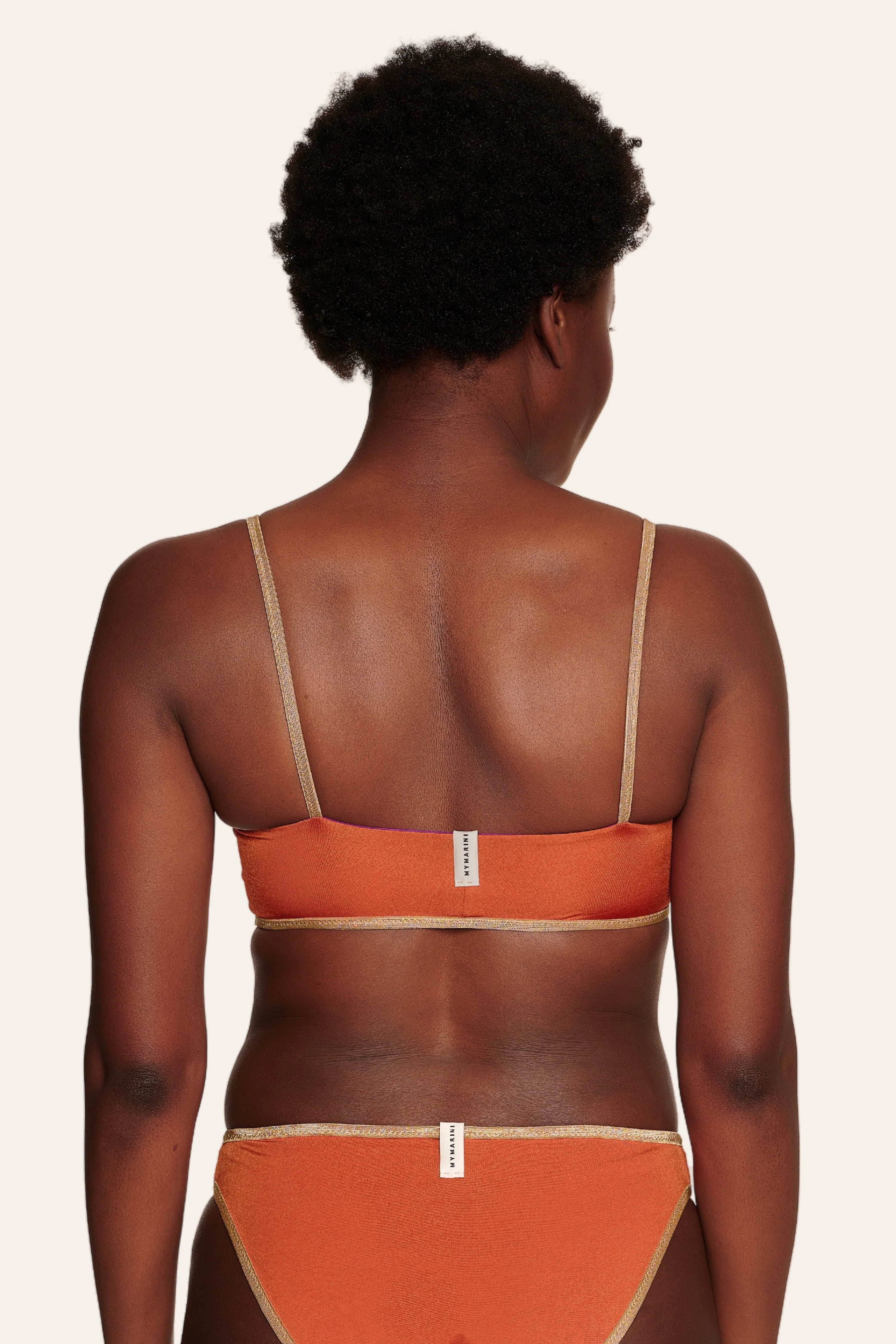 Rückansicht einer Person in einem MYMARINI Bikini mit Spaghettiträgern und hohem Beinausschnitt in Orange.#color_papaya-cassis