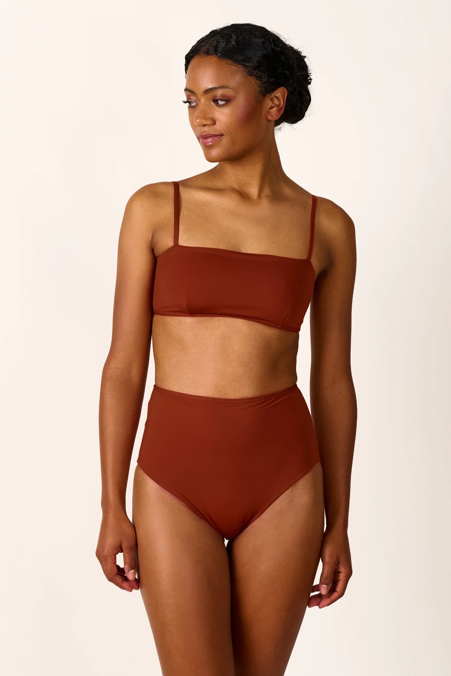 Frau trägt MYMARINI Bikini mit Spaghettiträgern und hoch geschnittener Bikinihose in Braun, schaut nach links.#color_sienna-orchid