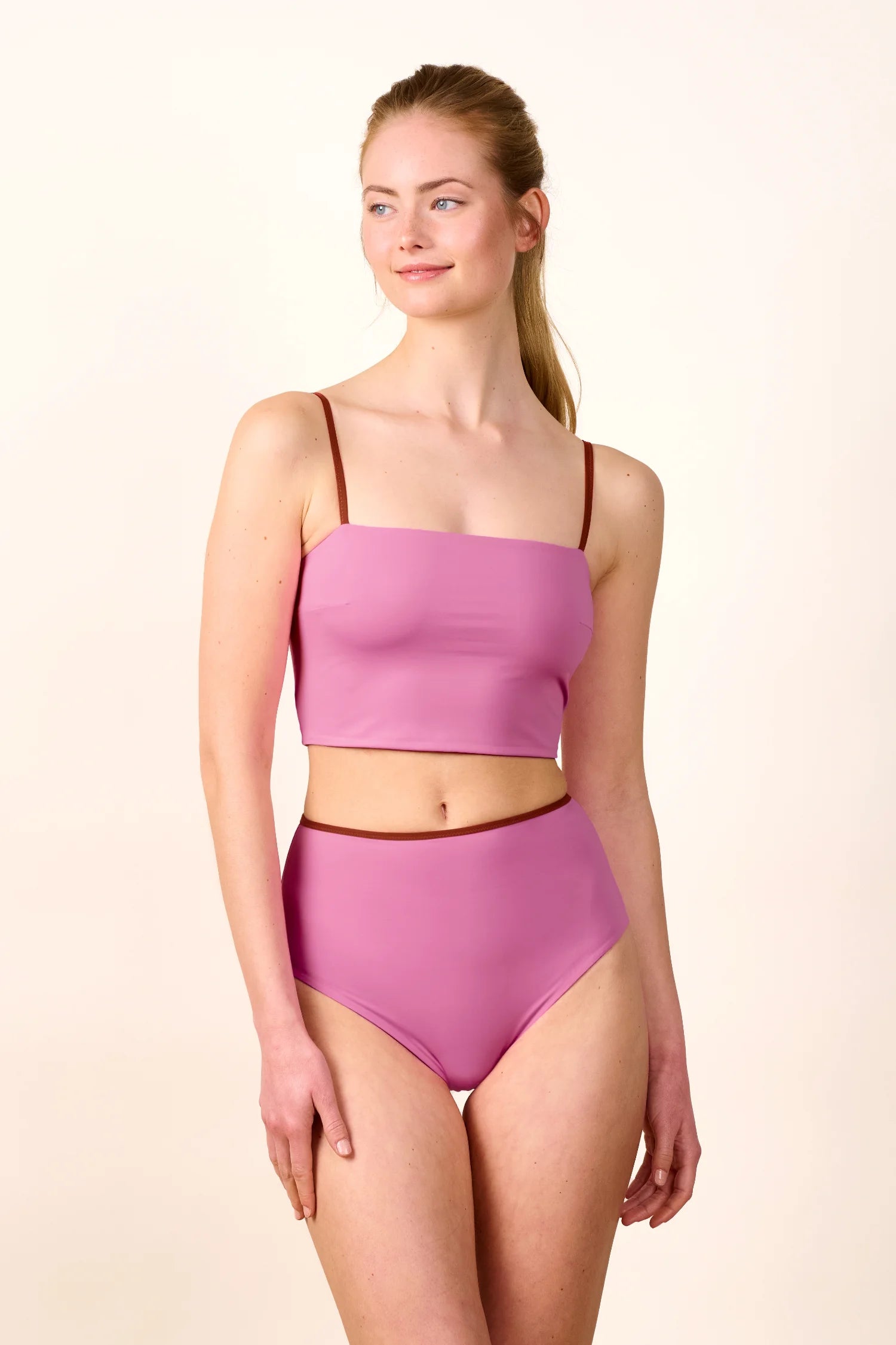 Frau trägt MYMARINI Bikini mit Bandeau-Top und High-Waist-Hose in Rosa, schmale Träger, lächelnd, vor hellem Hintergrund.#color_sienna-orchid