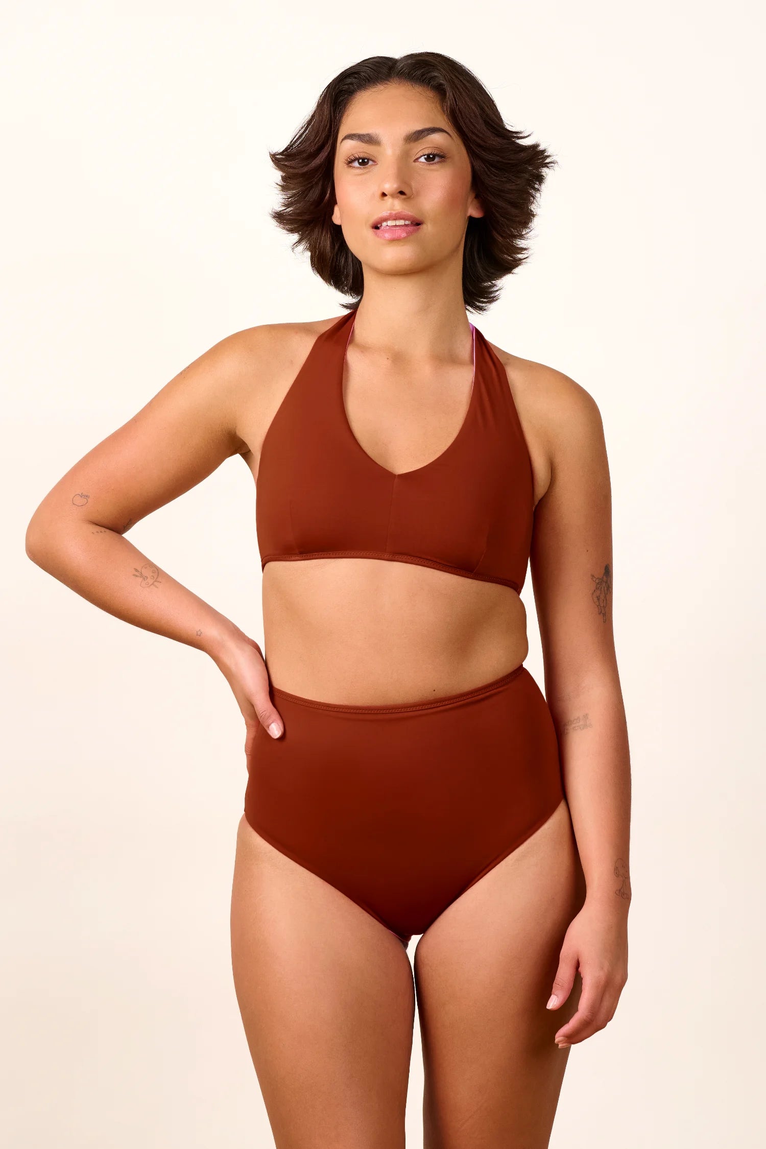 Frau trägt MYMARINI Bikini mit V-Ausschnitt und High Waist in Braun, lächelt in die Kamera vor neutralem Hintergrund.#color_sienna-orchid