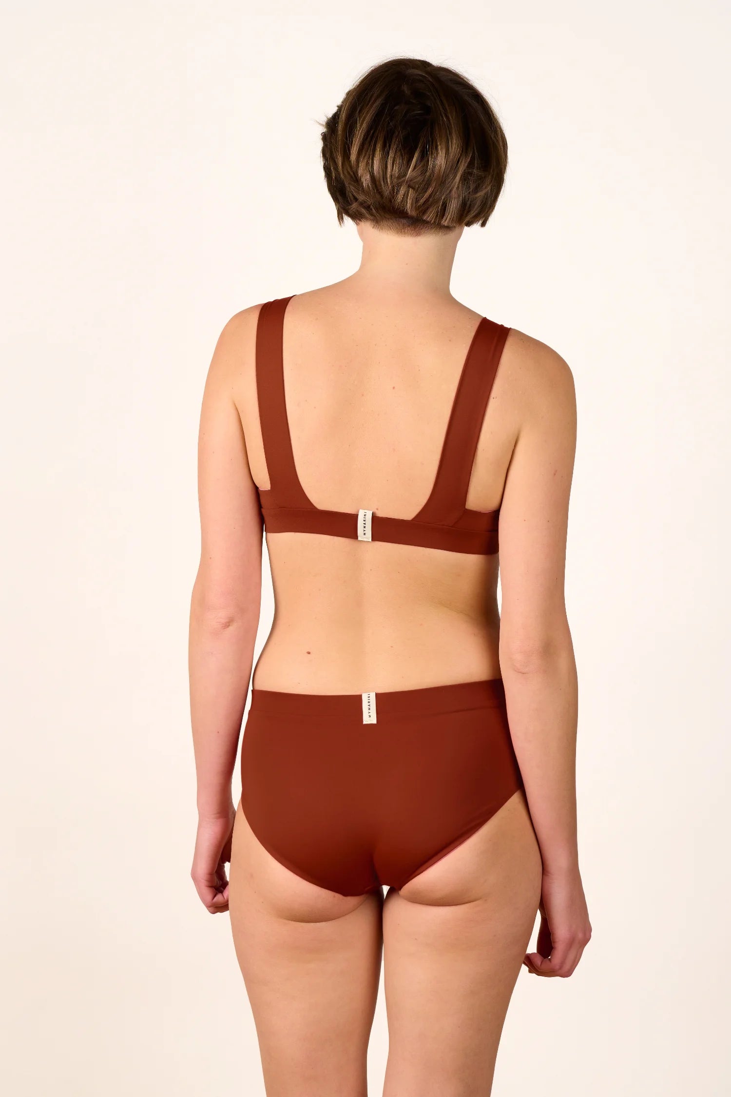 Rückansicht einer Person in MYMARINI Bikinihose und Bikinitop, beide hoch geschlossen, in Braun.#color_sienna-orchid