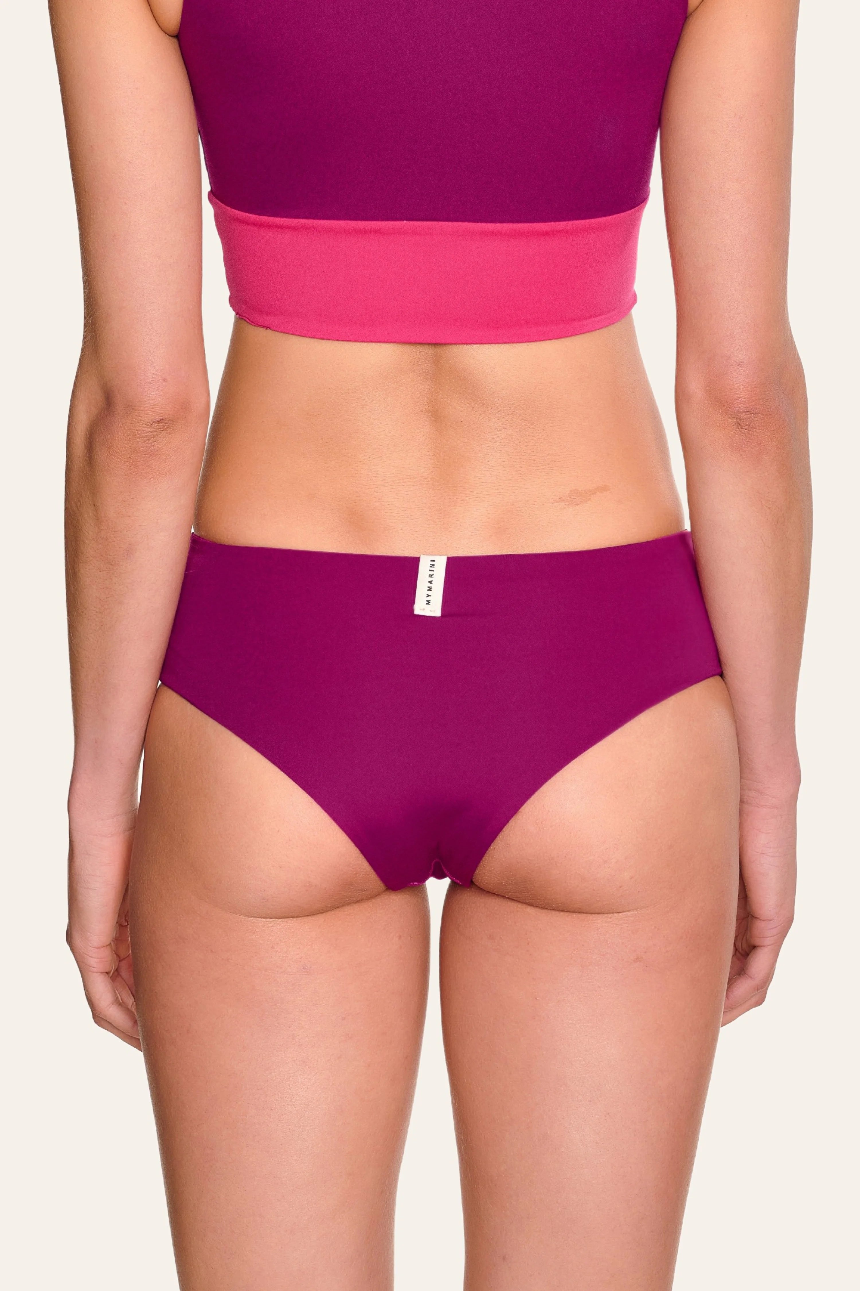 Rückansicht einer Person in MYMARINI Bikinihose mit hohem Beinausschnitt in Lila und pinkem Bikinitop.#color_pink-hortensia
