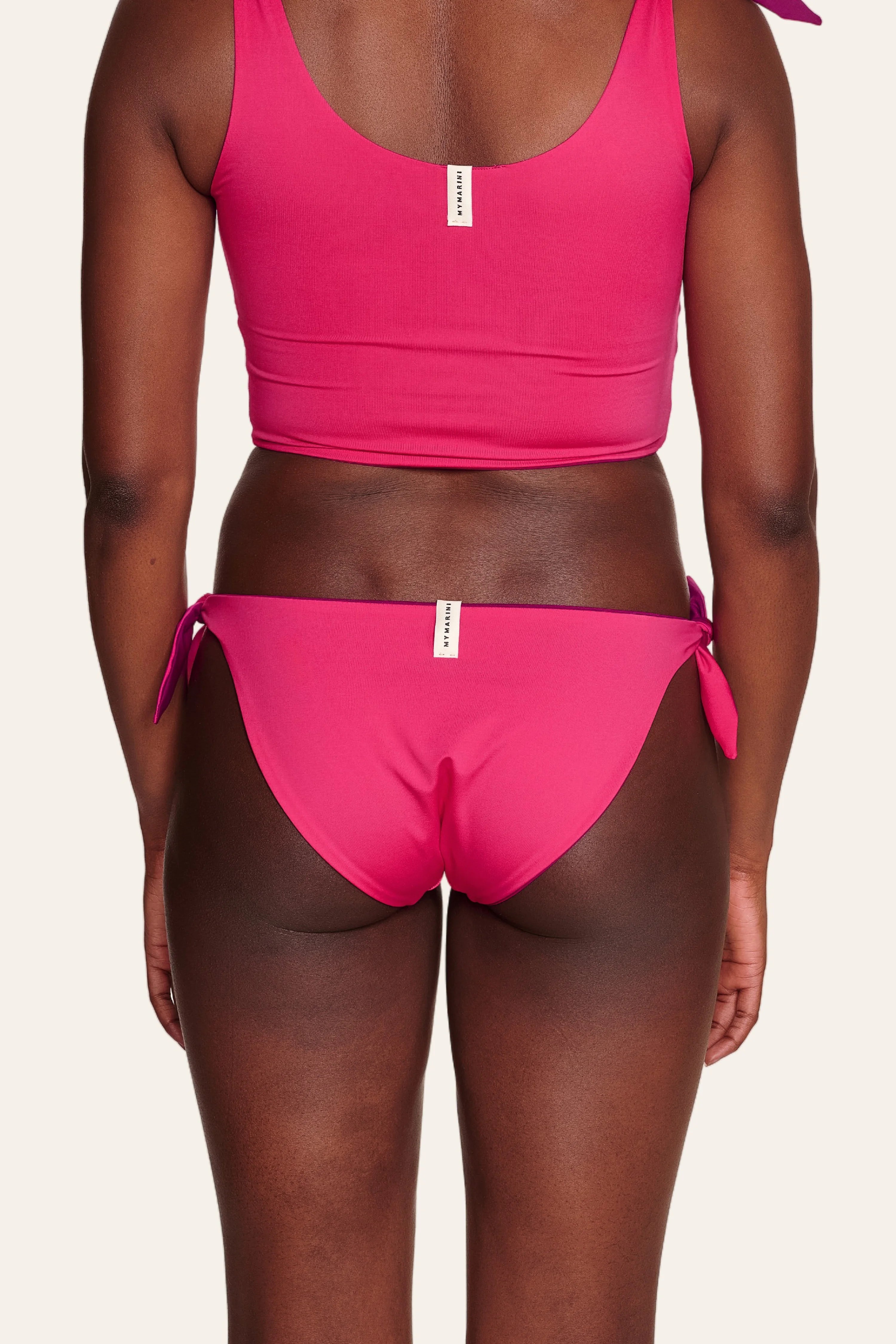 Rückansicht einer Person in einem pinken MYMARINI Bikinitop mit breiten Trägern und passender Bikinihose mit seitlichen Schleifen.#color_pink-hortensia