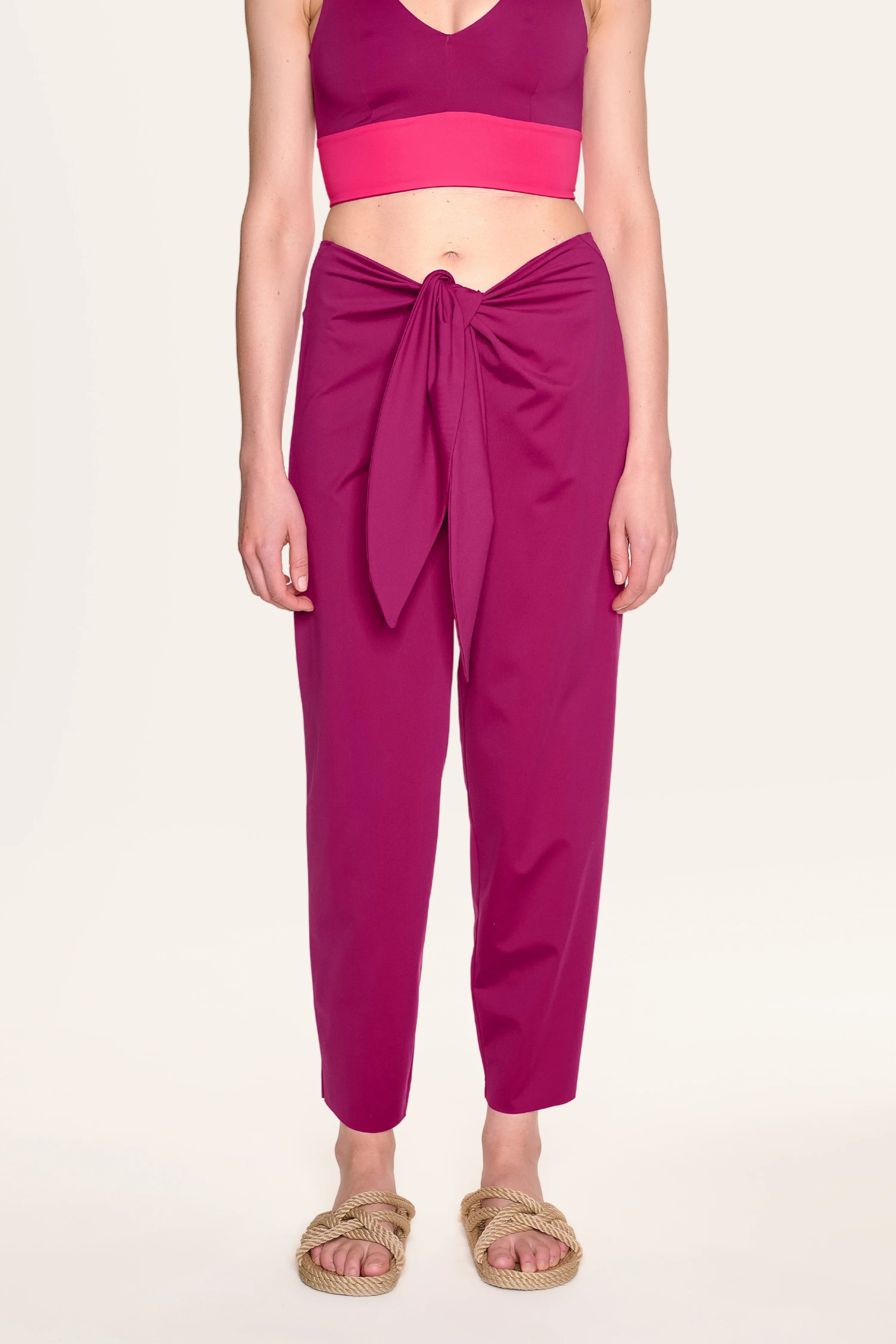 Frau in pinkem MYMARINI-Bikinitop mit V-Ausschnitt und passender Hose, stehend, mit Sandalen.#color_hortensia