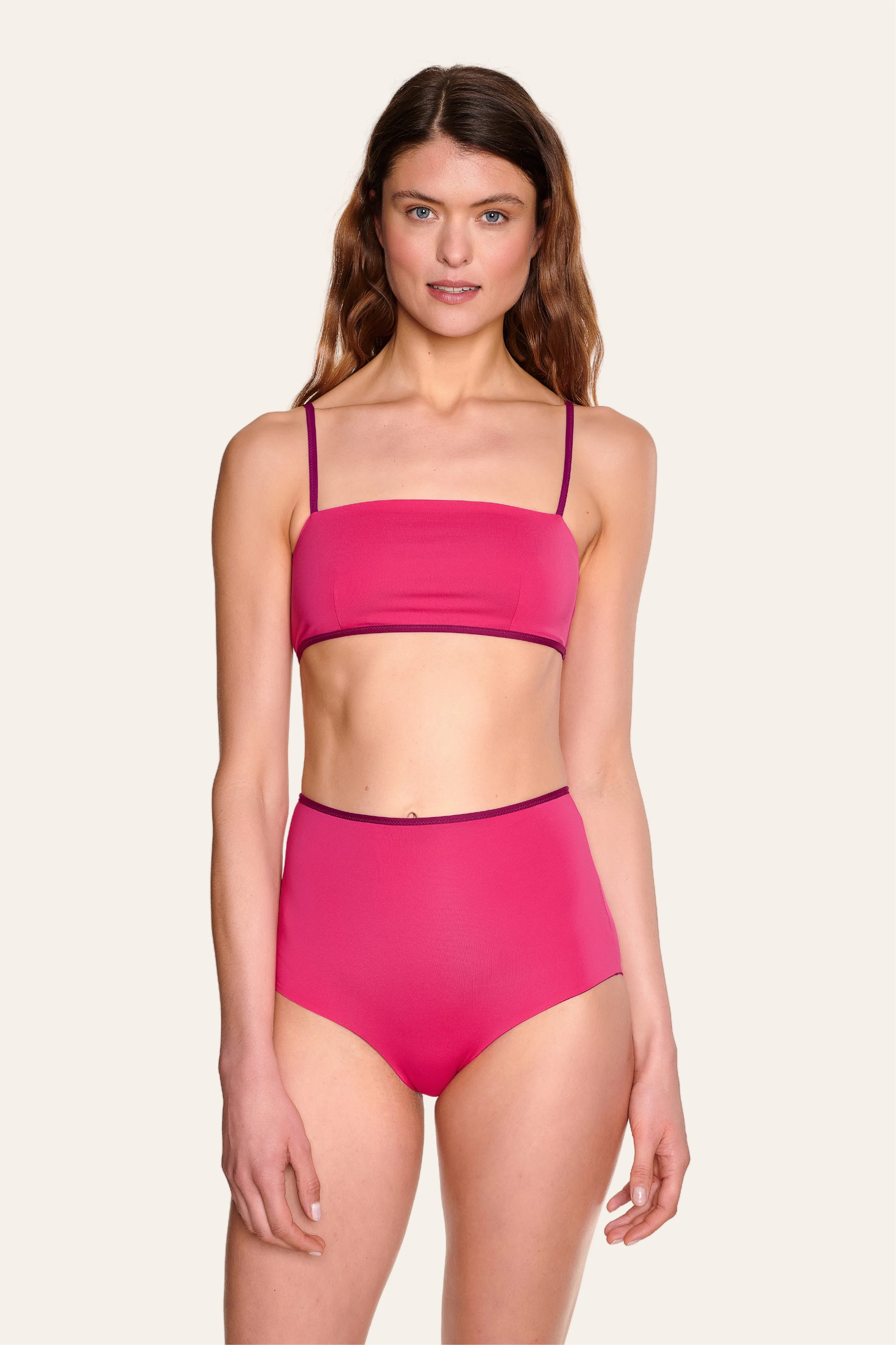 Frau trägt MYMARINI Bikini mit Bandeau-Top und High-Waist-Hose in Pink vor hellem Hintergrund.#color_pink-hortensia