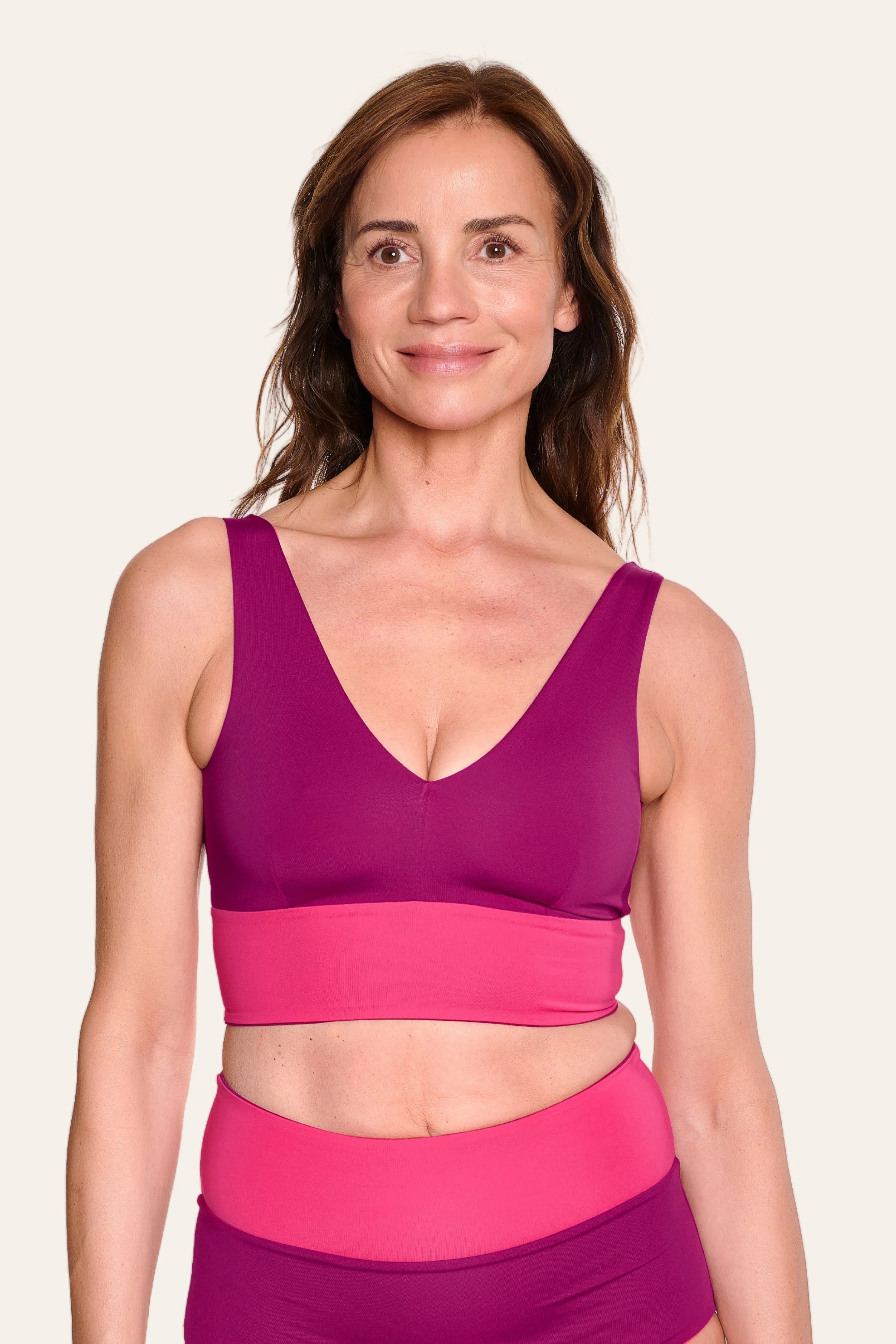 Frau trägt MYMARINI Bikinitop mit V-Ausschnitt und Bikinihose mit High Waist in Pink- und Violetttönen, lächelnd.#color_pink-hortensia