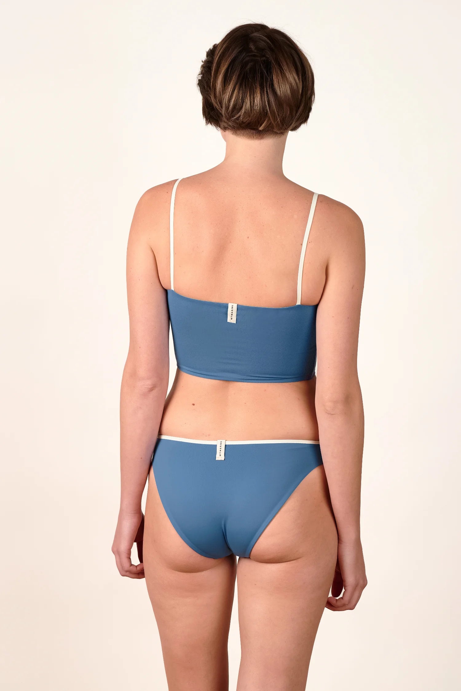 Frau in MYMARINI Bikinitop mit Spaghettiträgern und Bikinihose, Rückansicht, schlichtes Design in Blau mit weißen Akzenten.#color_coast-desert
