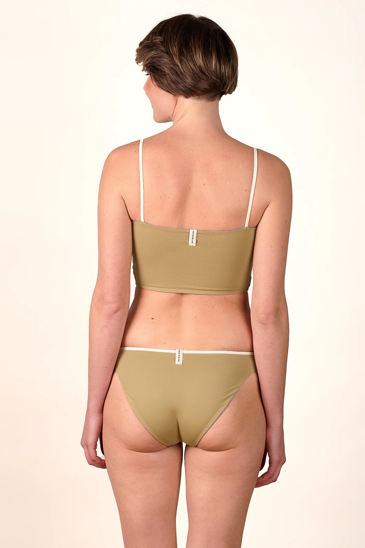 Rückansicht einer Frau in MYMARINI Bikinihose und Bikinitop mit Spaghettiträgern, beide in Olivgrün, hoher Beinausschnitt.#color_coast-desert