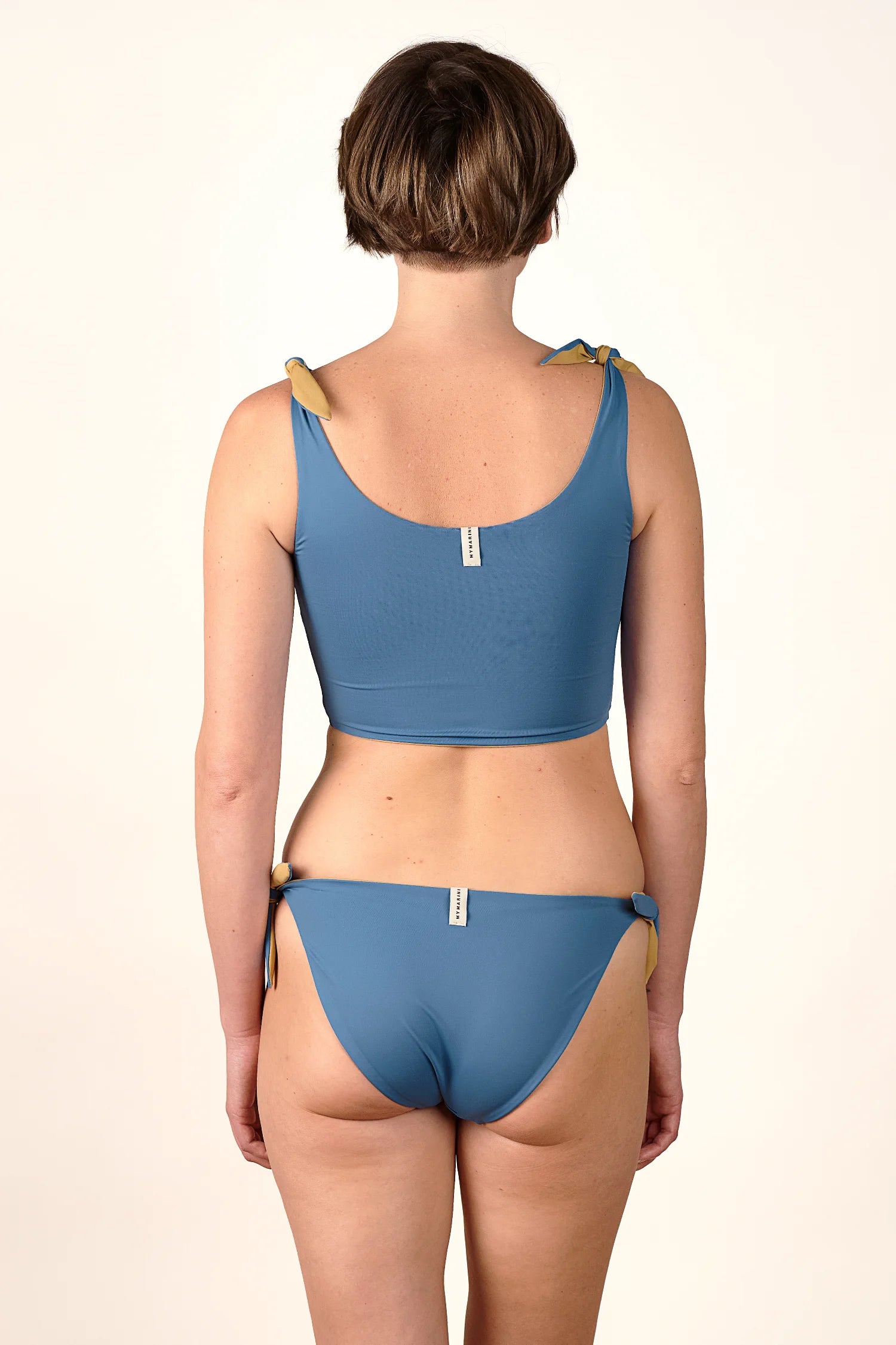 Frau in MYMARINI Bikini mit breiten Trägern und hohem Beinausschnitt, Rückansicht.#color_coast-desert