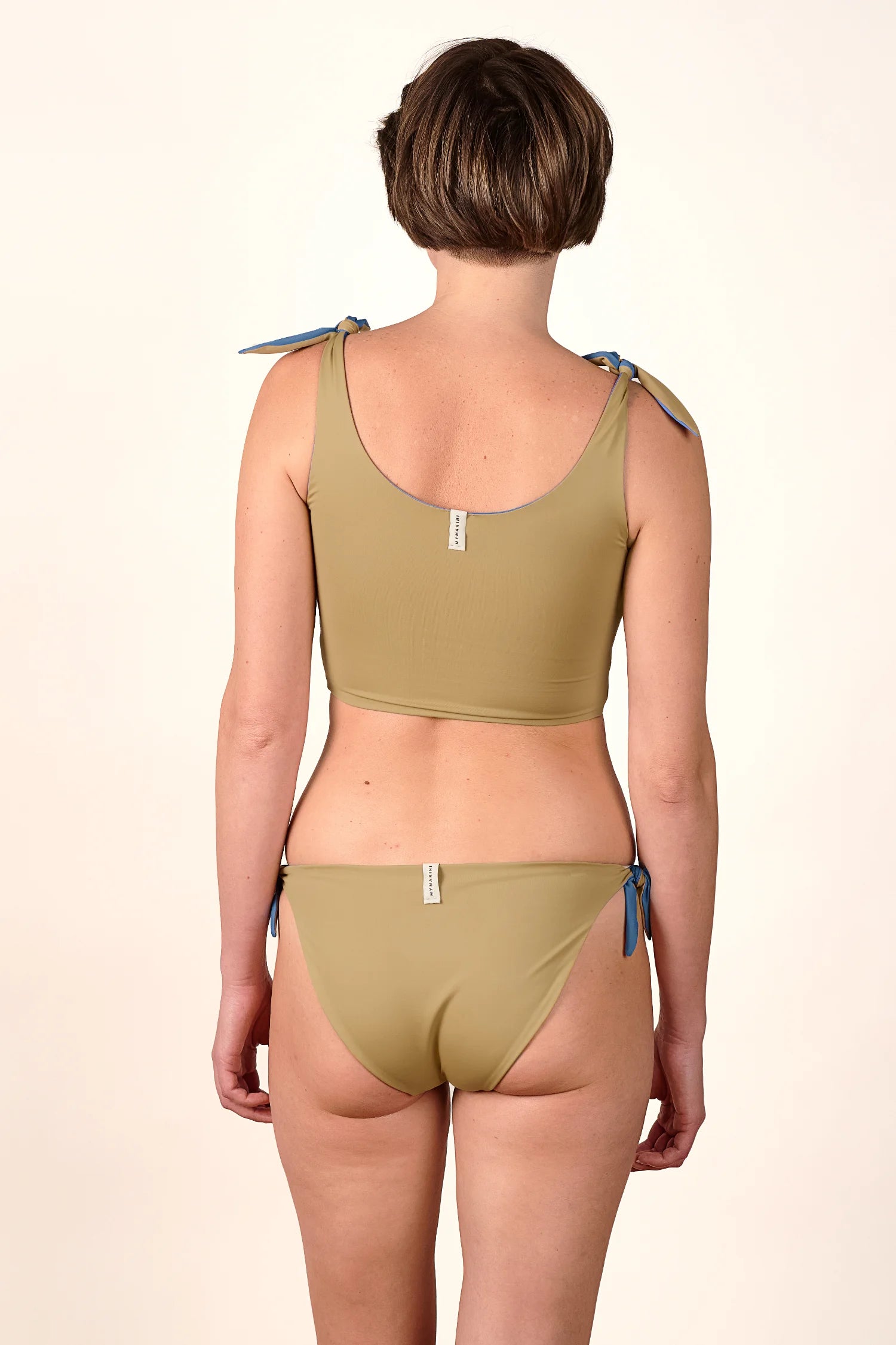 Rückansicht einer Person in einem MYMARINI Bikinitop mit breiten Trägern und Bikinihose mit hohem Beinausschnitt.#color_coast-desert