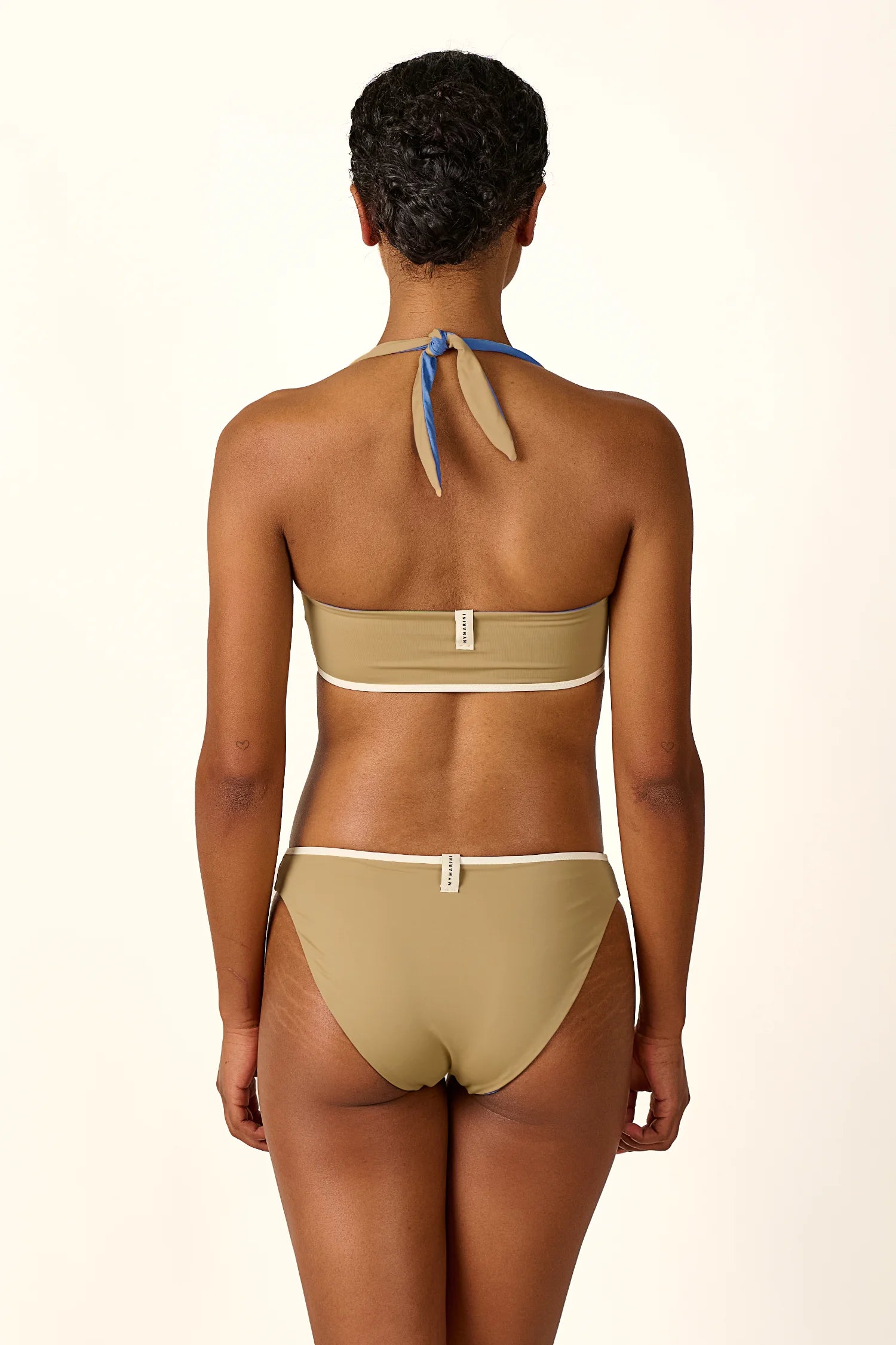 Rückansicht einer Person in einem MYMARINI Bikini mit Bandeau-Top und Bikinihose, beide in Beige, mit Neckholder-Träger.#color_coast-desert