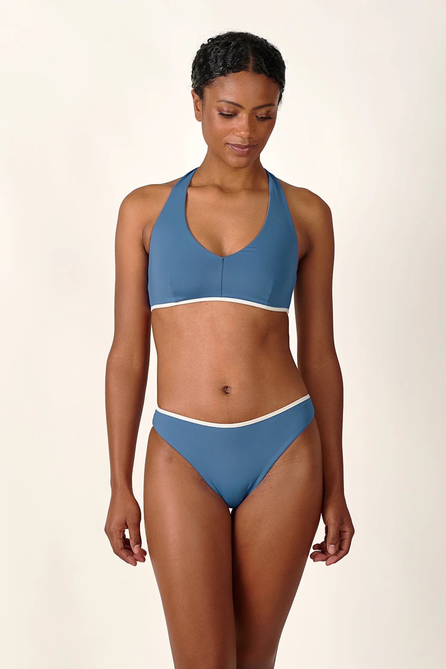 Frau trägt MYMARINI Bikini mit Neckholder-Top und Mid-Rise-Hose in Blau, lächelnd vor neutralem Hintergrund.#color_coast-desert