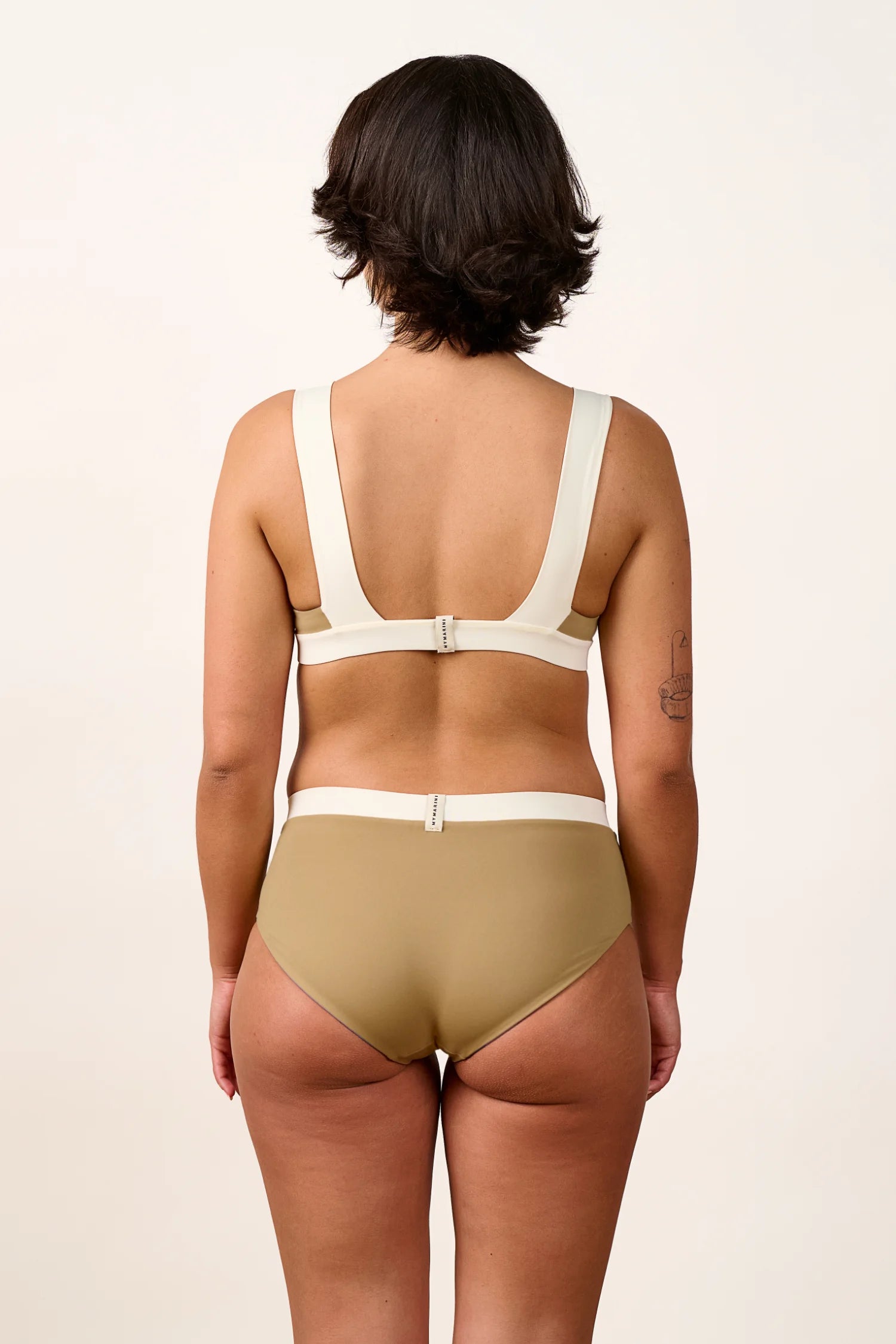 Rückansicht einer Frau in MYMARINI Bikinihose mit hohem Beinausschnitt und Bikinitop mit breiten Trägern.#color_coast-desert