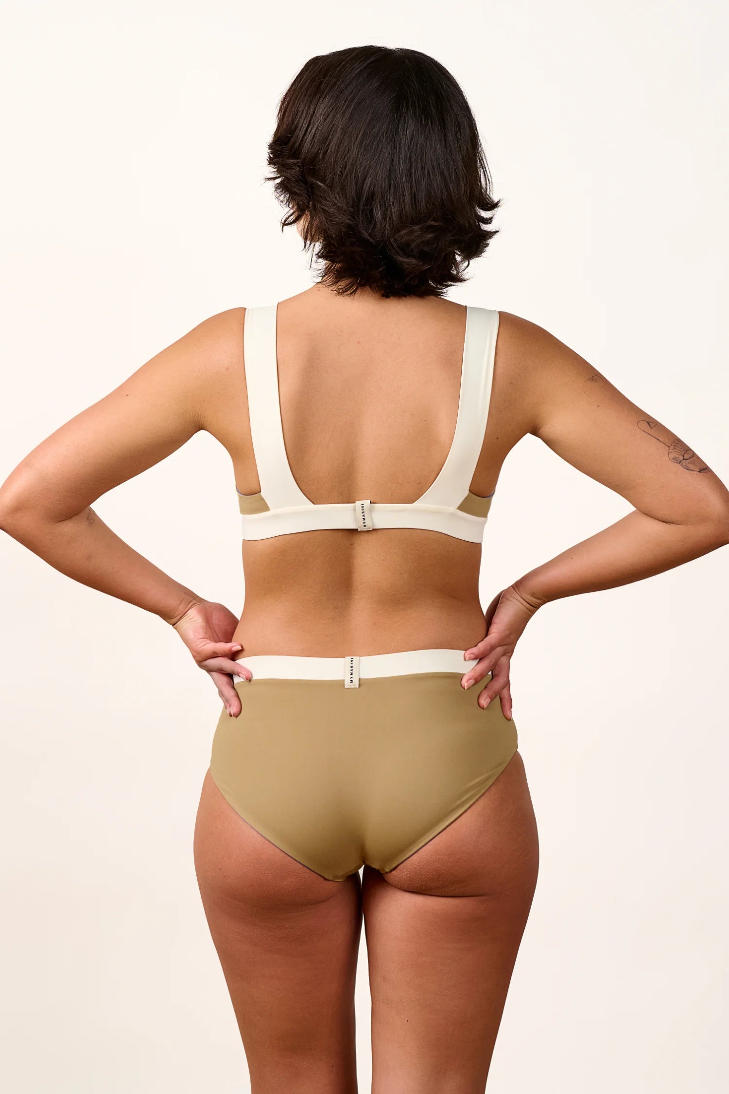Rückansicht einer Frau in MYMARINI Bikinihose mit hohem Beinausschnitt und Bikinitop mit breiten Trägern.#color_coast-desert
