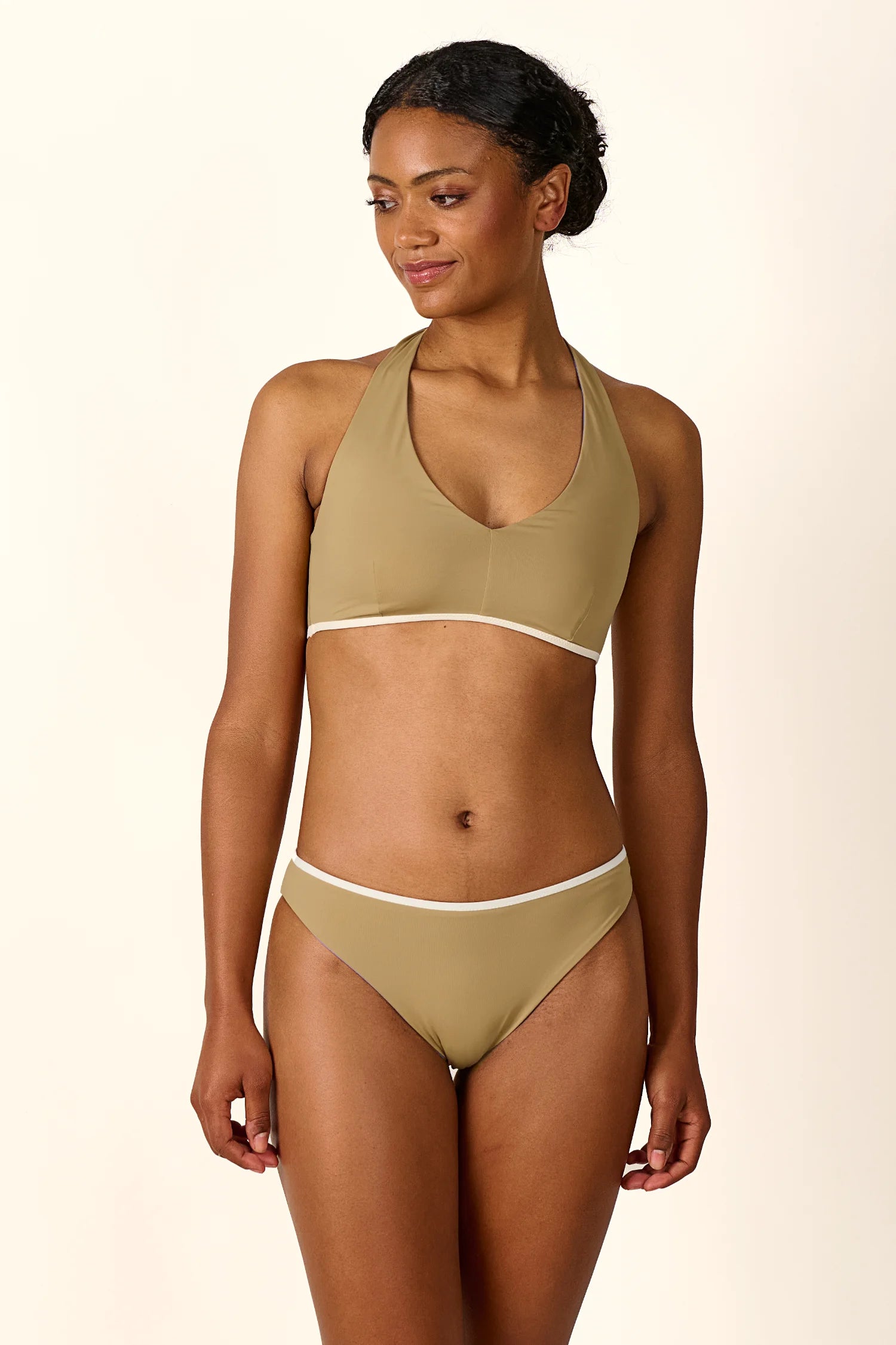 Frau trägt MYMARINI Bikini mit Neckholder-Top und Mid-rise Hose in Beige. Sie blickt zur Seite und lächelt leicht.#color_coast-desert
