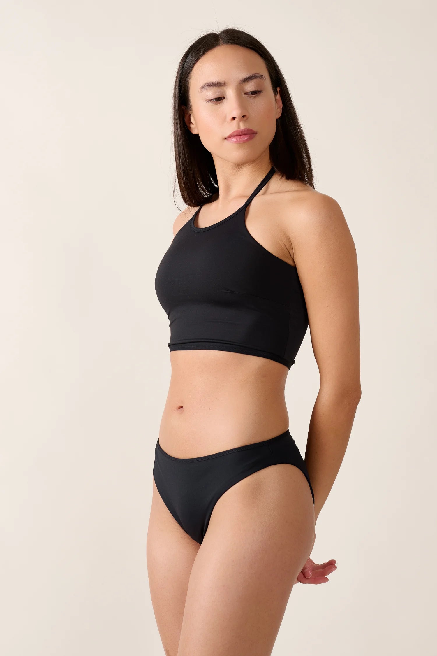 Frau trägt schwarzen MYMARINI Bikini mit hochgeschlossenem Top und hohem Beinausschnitt, vor neutralem Hintergrund.#color_black-navy
